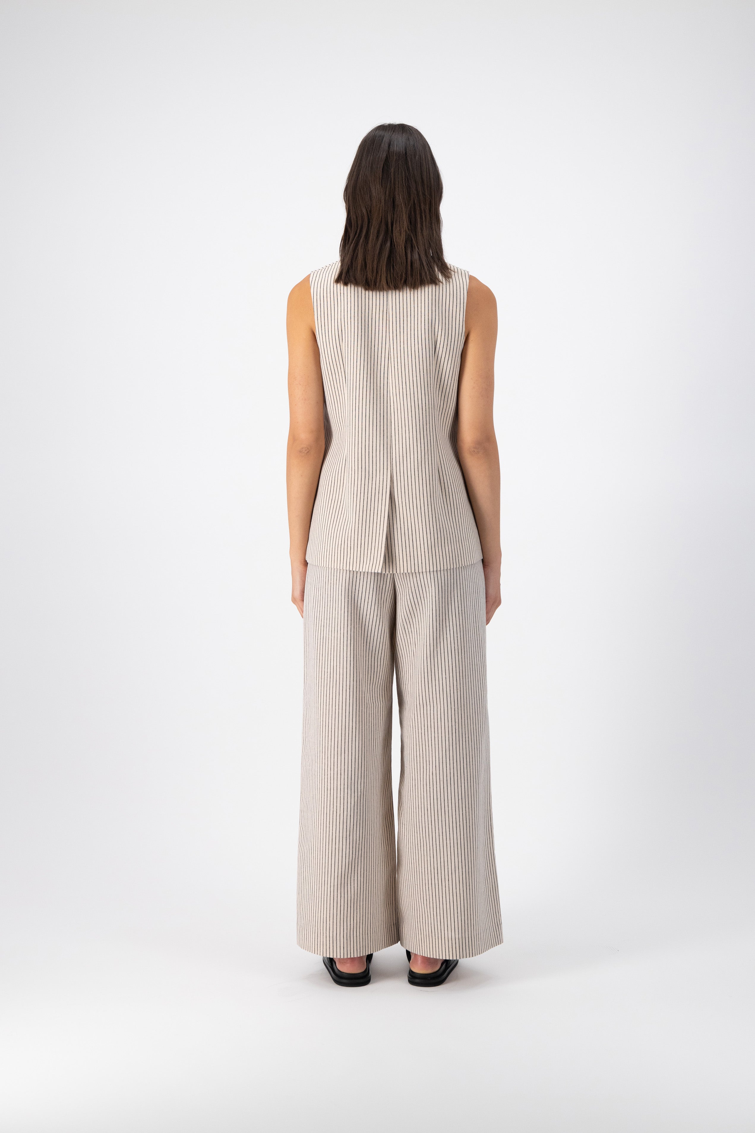 Back view of a woman wearing a Hayes Linen Stripe Vest paired with wide-leg pants in the same color. The vest is fully lined with a center back vent.