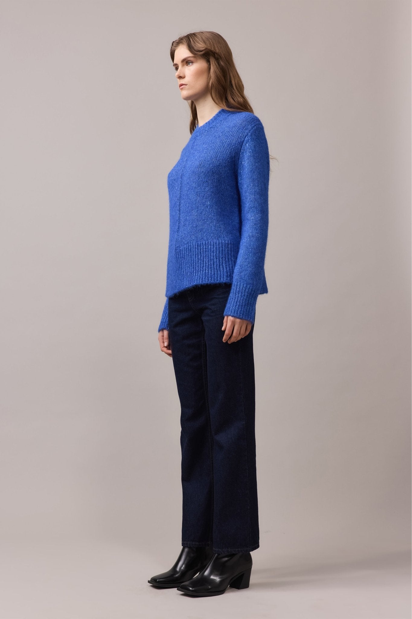 Side view of a woman in the Alfie Alpaca Cotton Knit, featuring a textured dropped-needle detail and ribbed hem, styled with dark straight-leg jeans.
