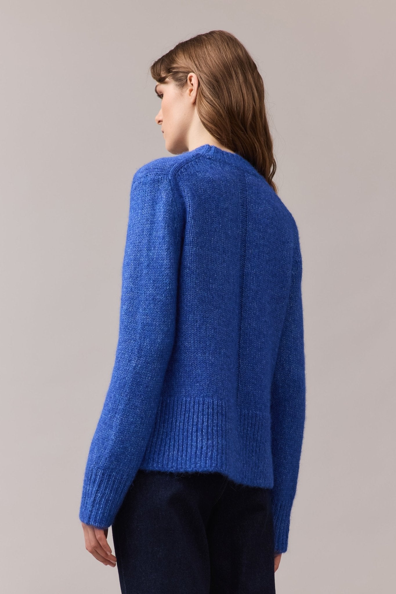 Three-quarter back view of a woman in the cobalt blue Alfie Lofty Knit, showing the ribbed hem and back seam detail in soft alpaca-cotton blend.