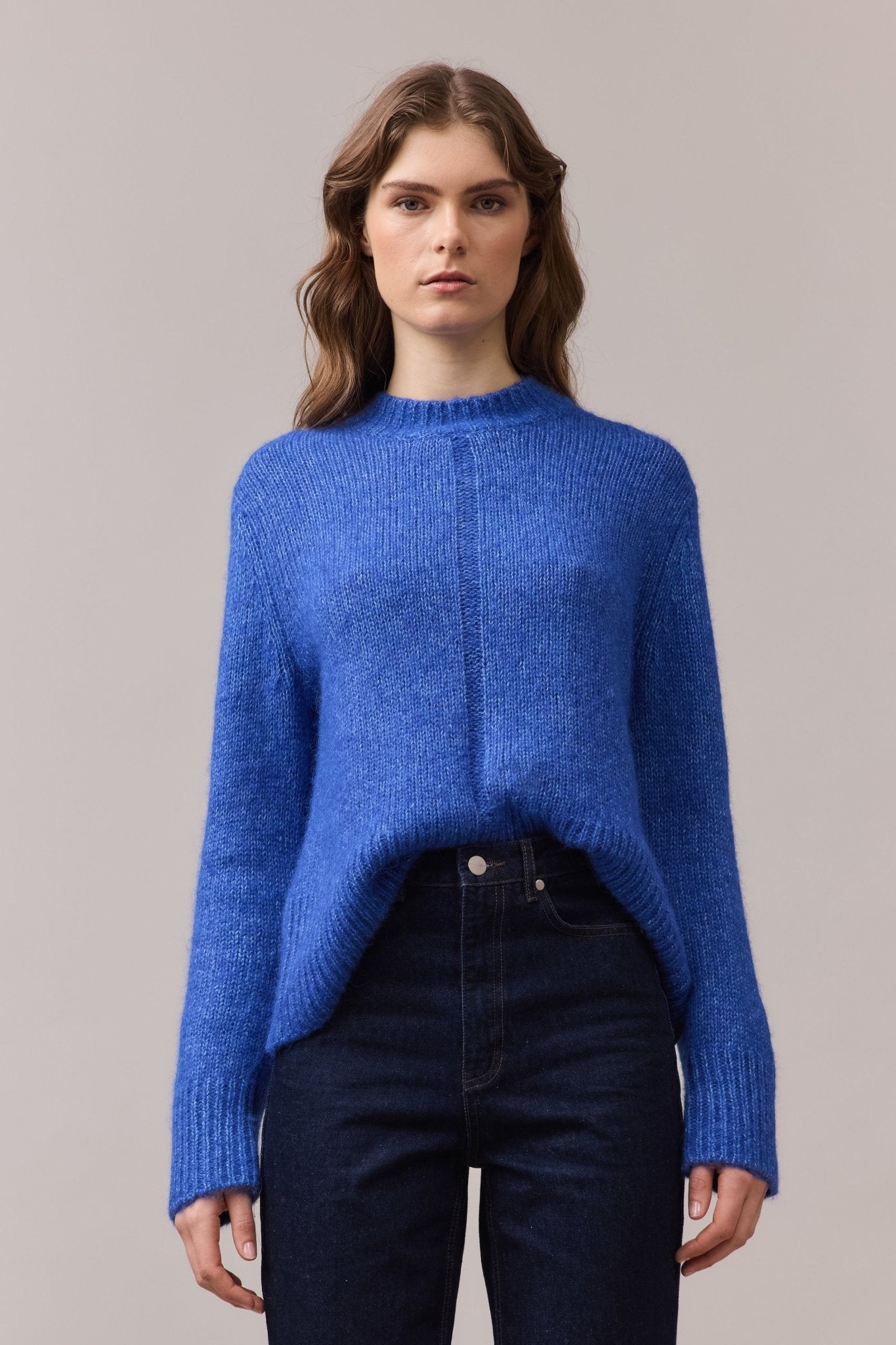 Woman wearing the Alfie Alpaca Cotton Knit in cobalt blue, styled with a front tuck into high-rise jeans, highlighting the ribbed hem and soft drape.