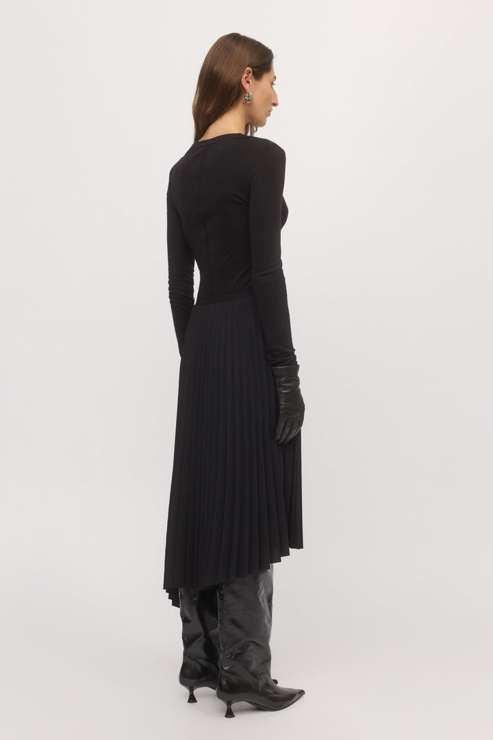Back full-body view of woman in black Asymmetric Pleat Skirt paired with heels – highlighting flow and shape.