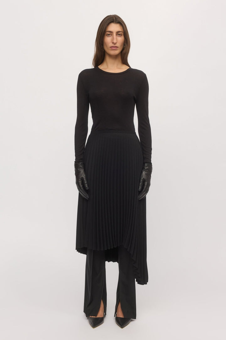 Woman wearing black Asymmetric Pleat Skirt with fitted top and knee-high boots