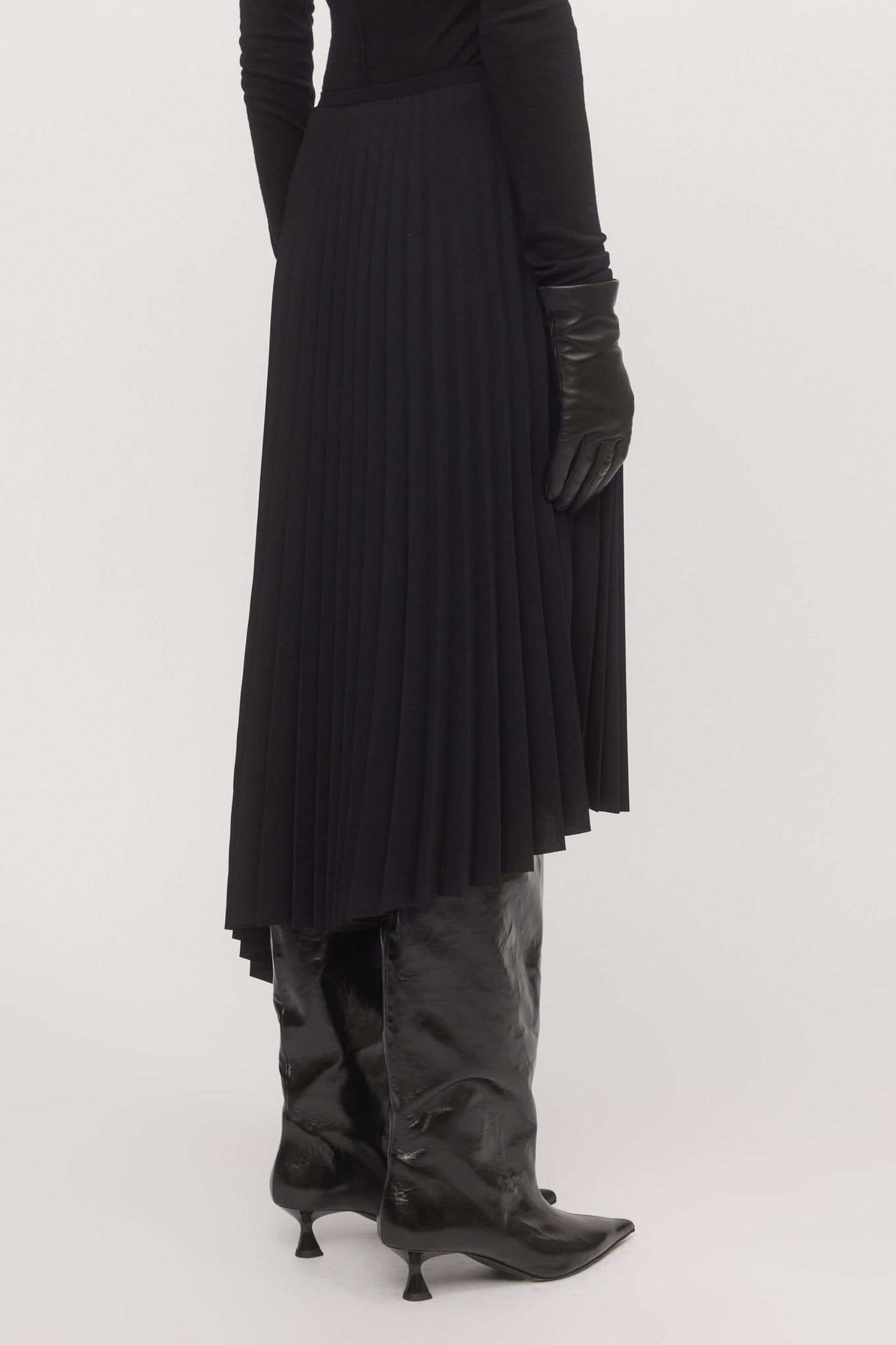 Close-up of pleated black Asymmetric Pleat Skirt from behind, highlighting asymmetry and fabric texture.