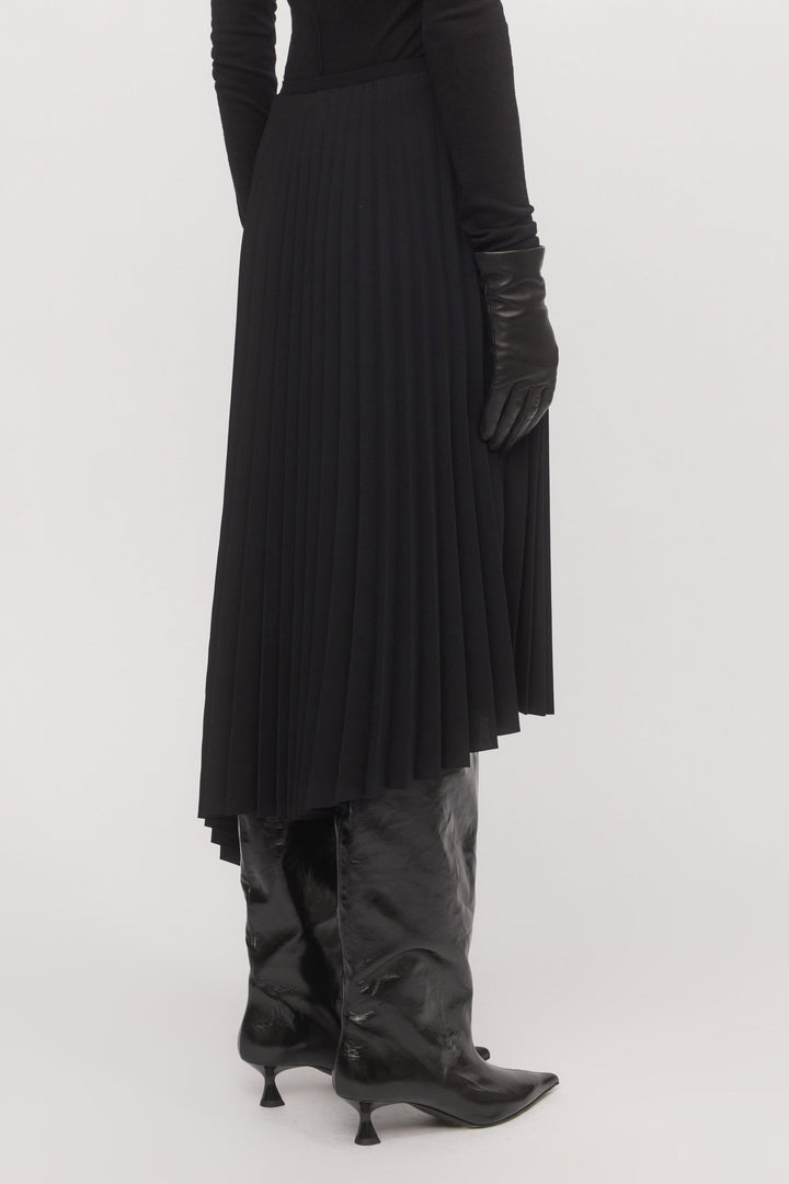 Close-up of pleated black Asymmetric Pleat Skirt from behind, highlighting asymmetry and fabric texture.