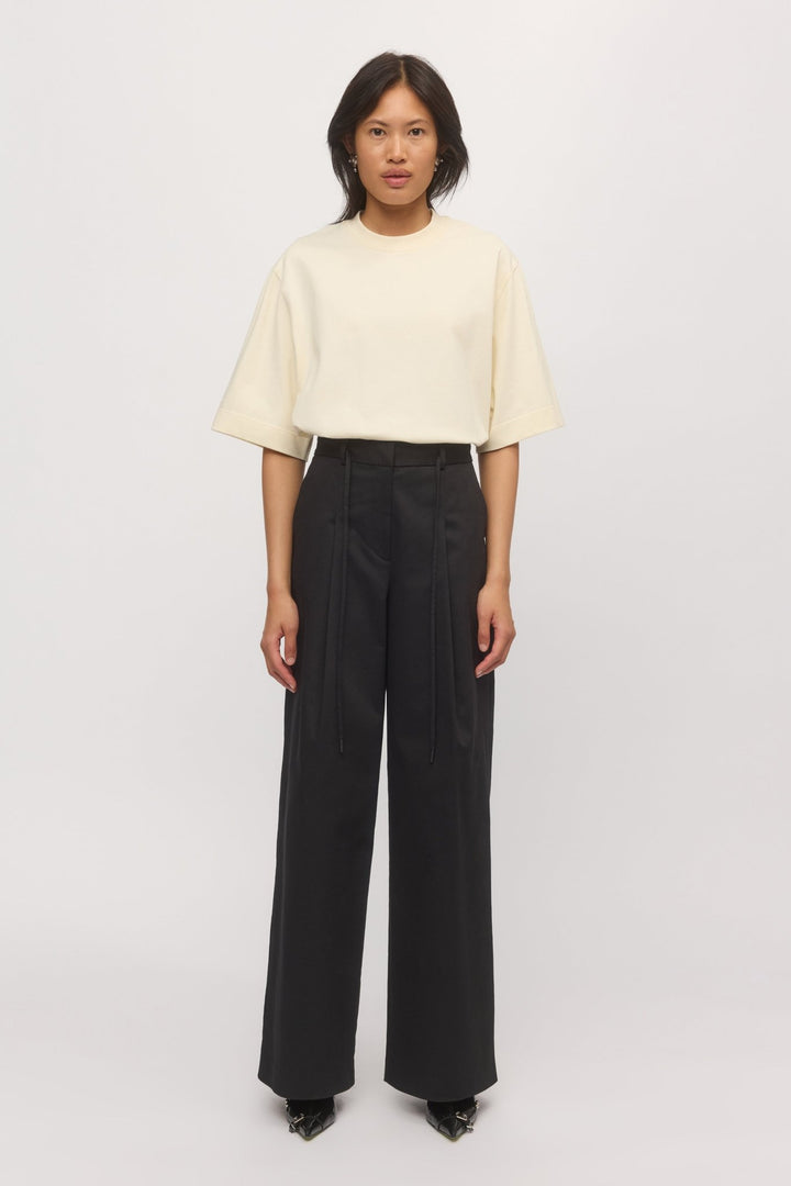 Woman wearing the Boyfriend Tee in Natural, partially tucked into high-waisted black trousers for a clean, modern silhouette with relaxed ease.