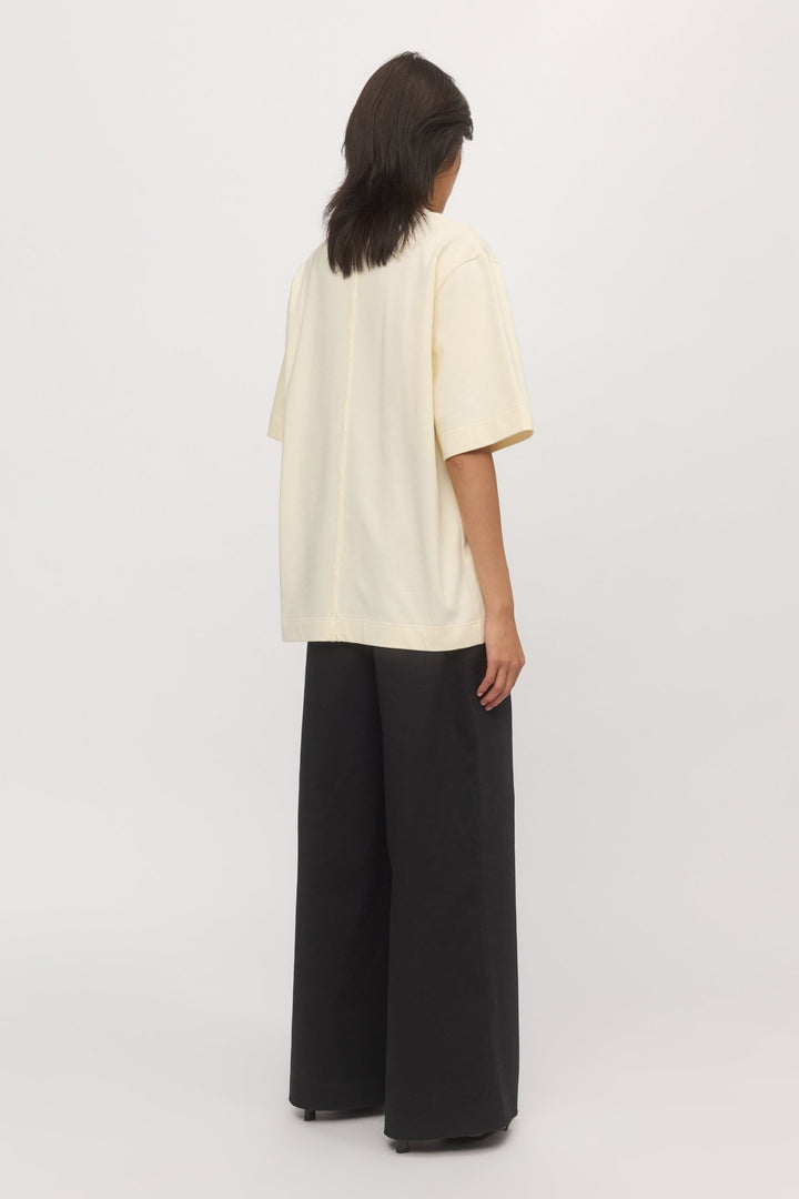 Back view of a woman wearing the Boyfriend Tee in Natural, highlighting the wide hem and straight seam detail in a softly structured cotton jersey.