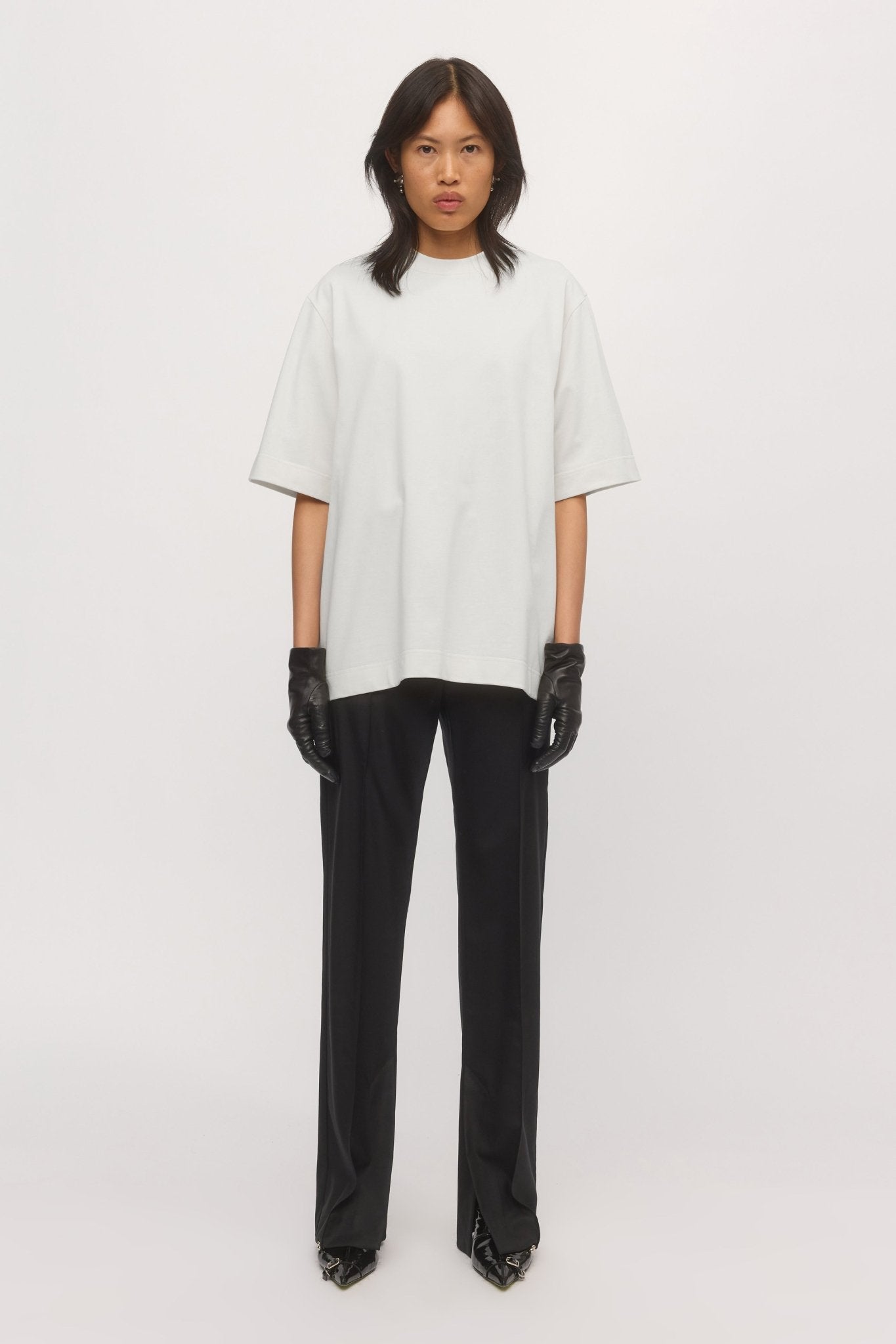 Woman wearing the Boyfriend Tee in White – oversized cotton t-shirt with relaxed fit, styled with black trousers and gloves.