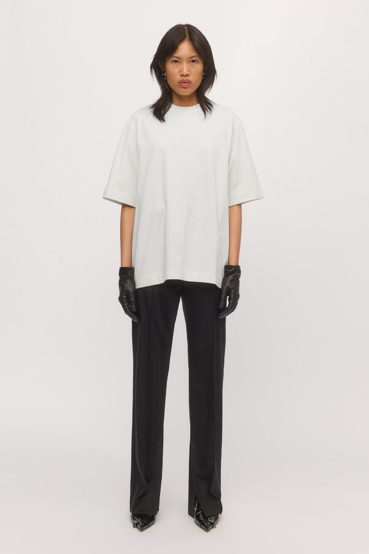 Woman wearing the Boyfriend Tee in White – oversized cotton t-shirt with relaxed fit, styled with black trousers and gloves.