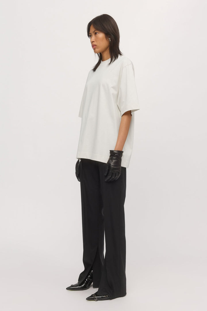 Side view of woman in White Boyfriend Tee – slouchy silhouette and short sleeves, paired with black trousers.