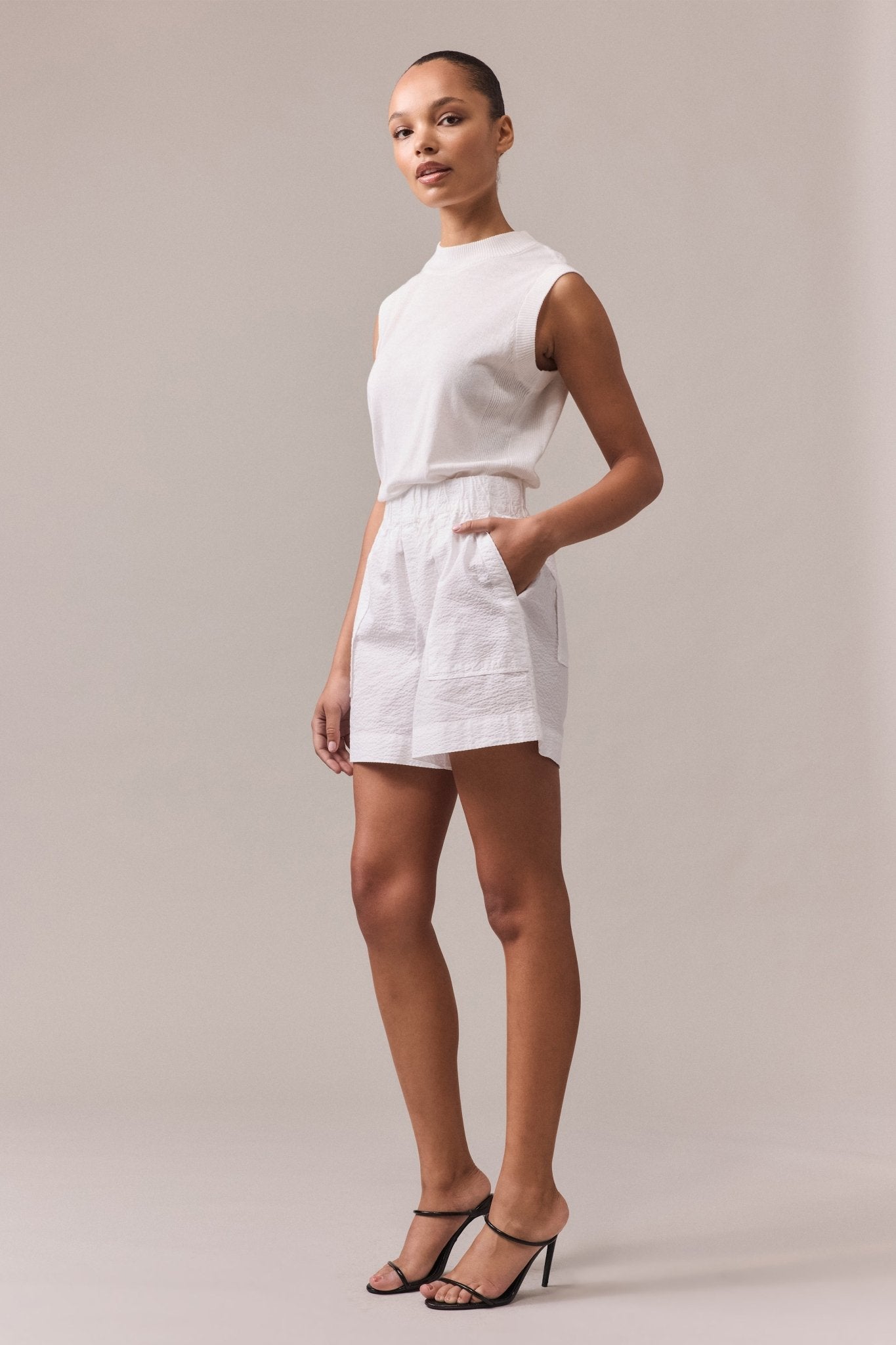 Side view of a woman is wearing white Crawford textured cotton shorts with white knit top.