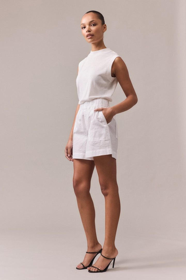Side view of a woman is wearing white Crawford textured cotton shorts with white knit top.