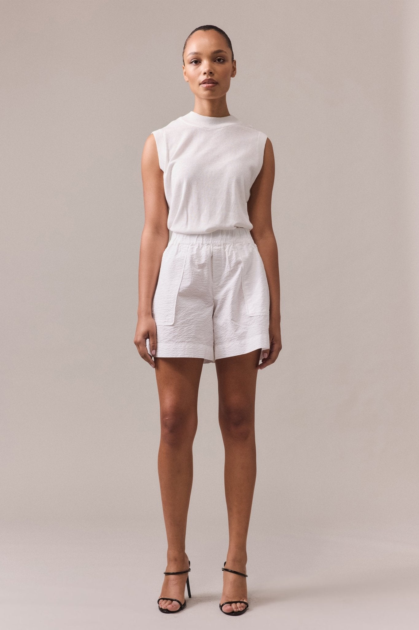 A woman is wearing white Crawford textured cotton shorts with white knit top.