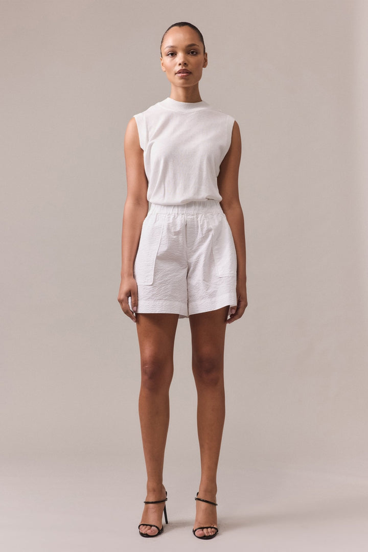 A woman is wearing white Crawford textured cotton shorts with white knit top.