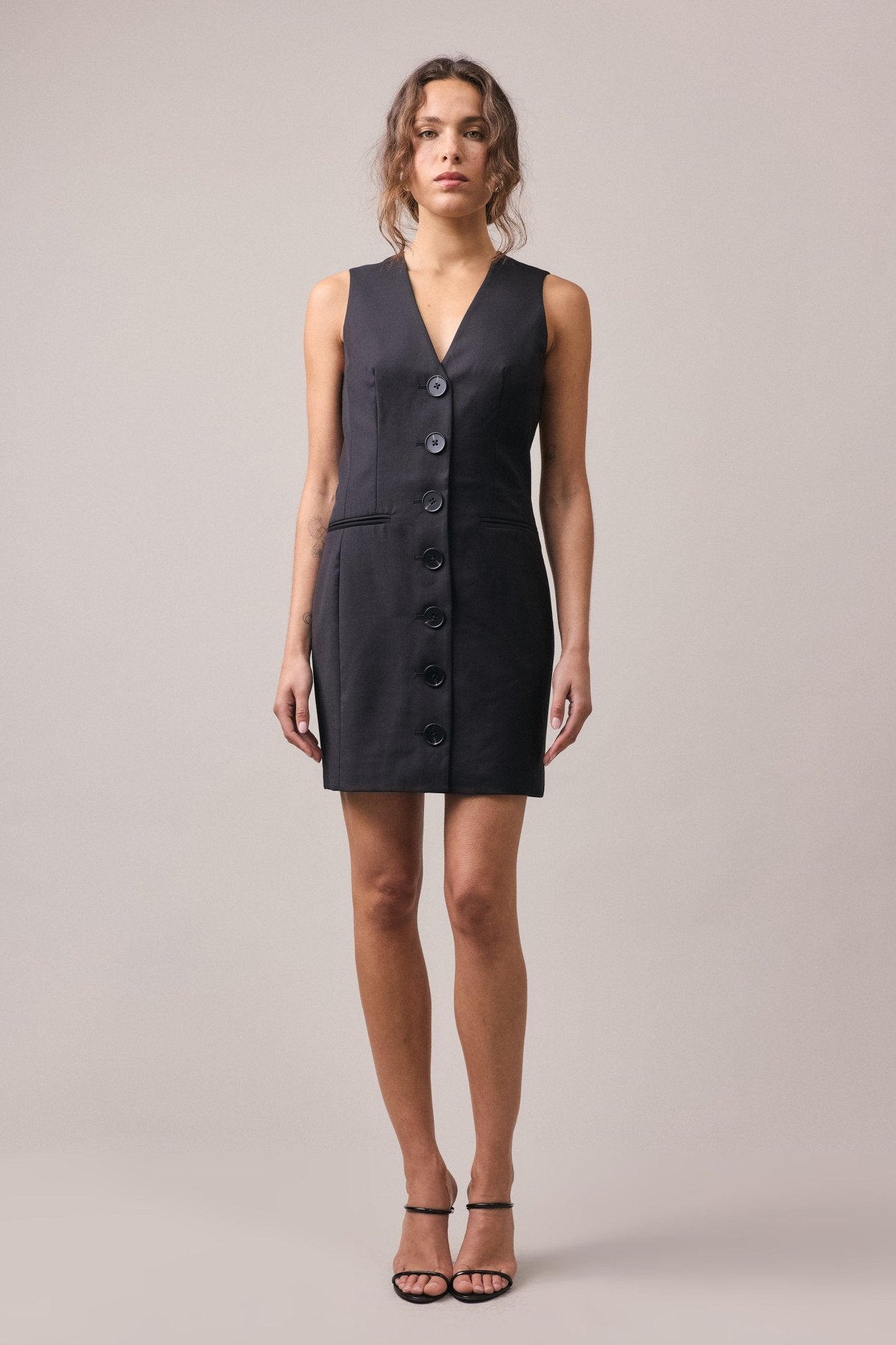 A woman wearing the Havana Tailored Dress in black, a mini dress crafted from lightweight 100% wool, featuring a fitted bust, waist, and slight A-line hem.
