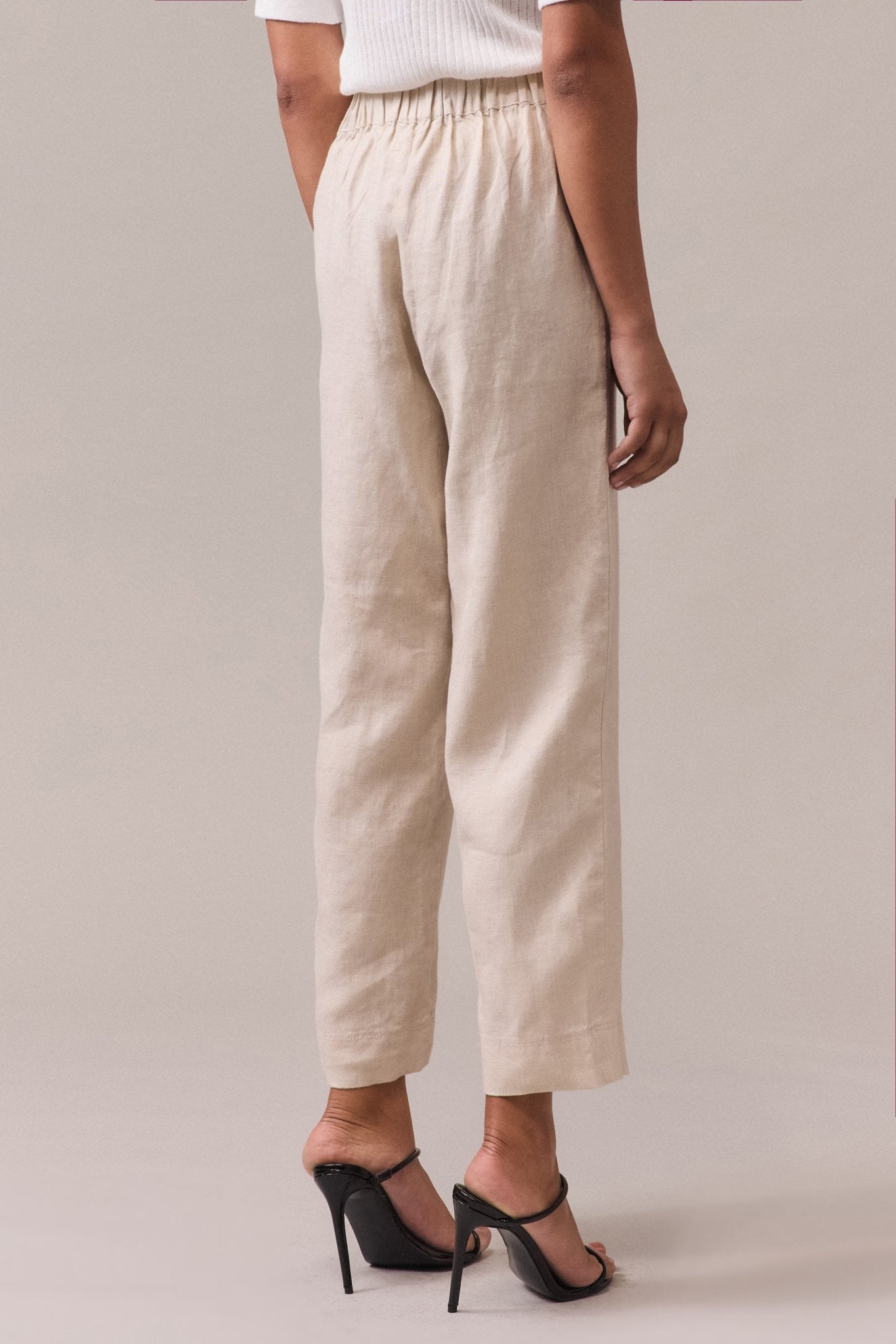 A woman seen from the back, wearing sand linen pants with an elasticated back waist.