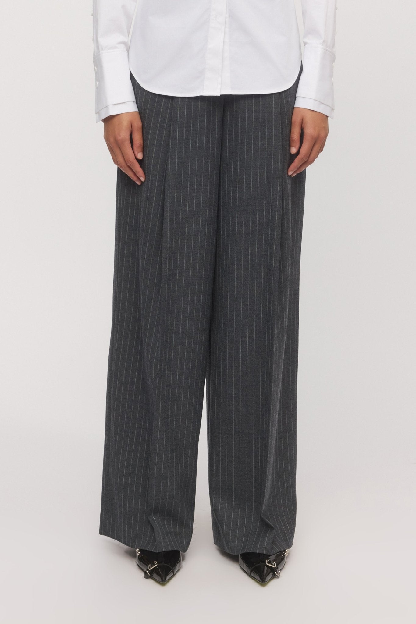 Close-up of a woman wearing the Lola Wide Leg Pant in graphite stripe with a white shirt, showcasing the relaxed silhouette and front pleats. - Skin and Threads