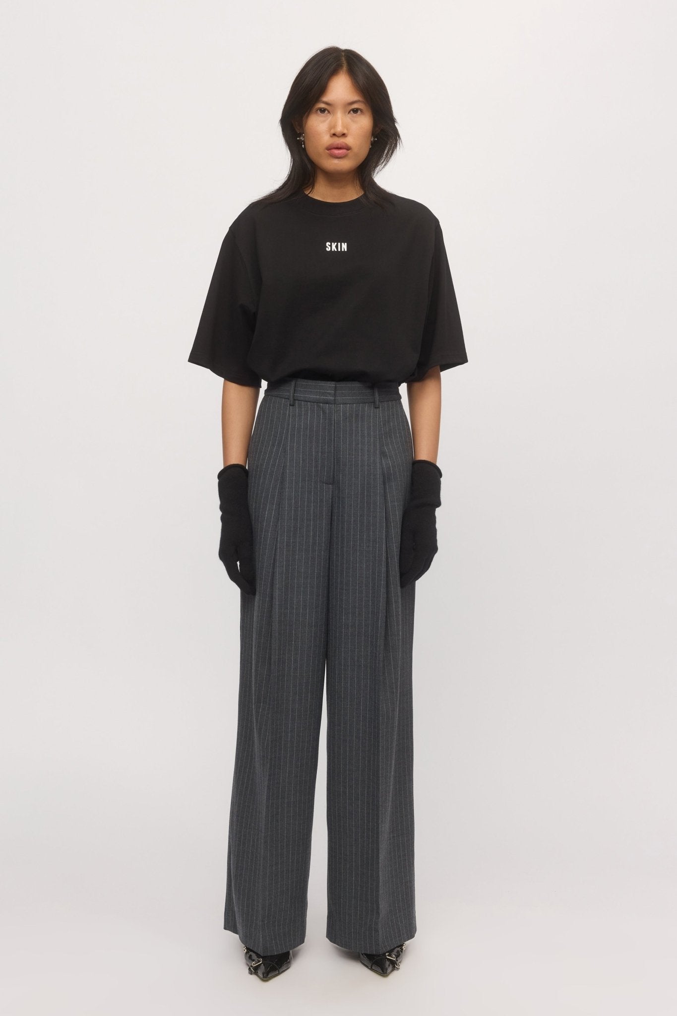 A woman wearing graphite pinstripe Lola Wide Leg Pants styled with a black oversized SKIN t-shirt and black gloves. - Skin and Threads