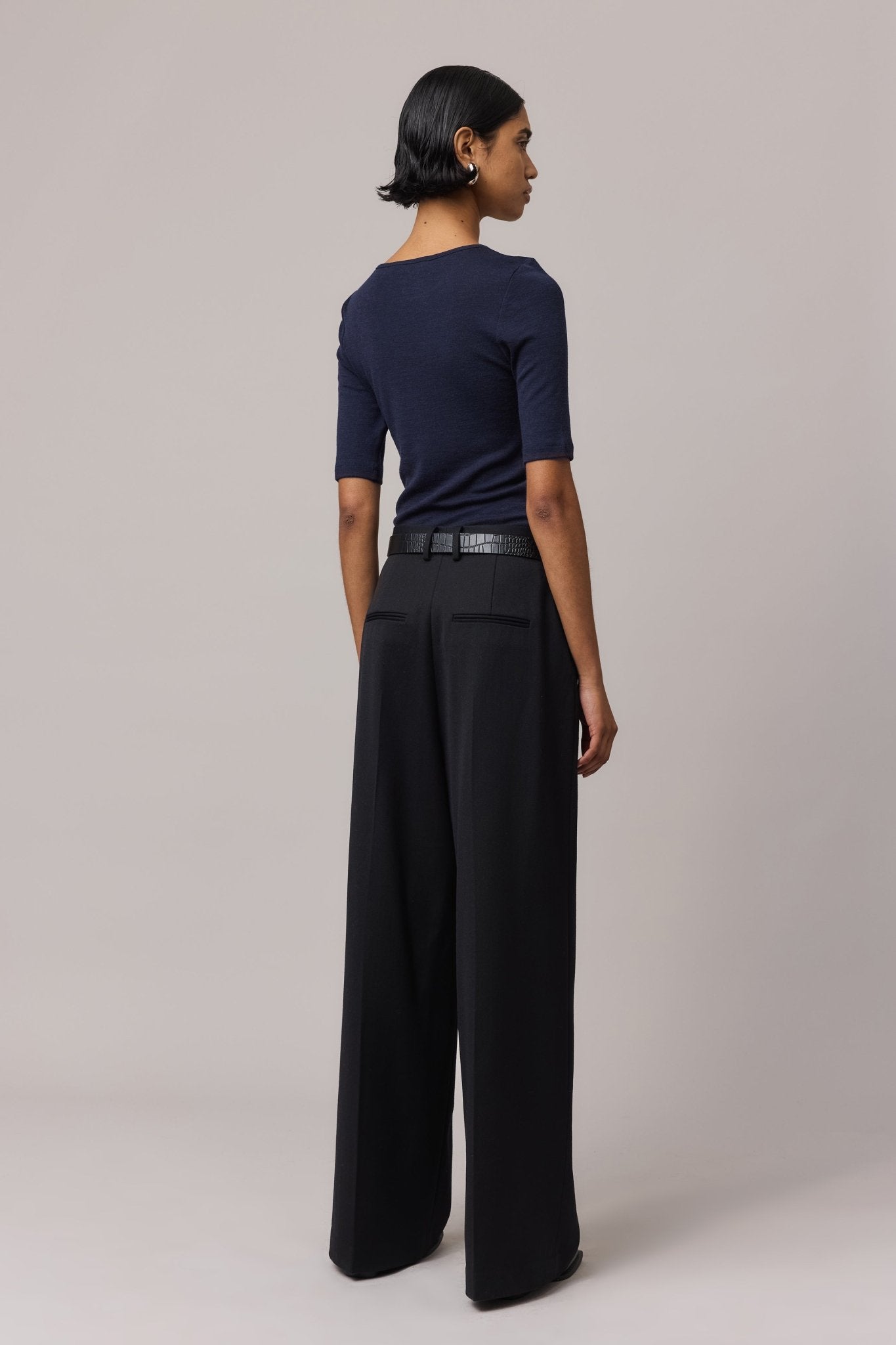 View from behind of a woman wearing an indigo Merino Wool Crew Neck Tee with elbow sleeves and black linen pants.