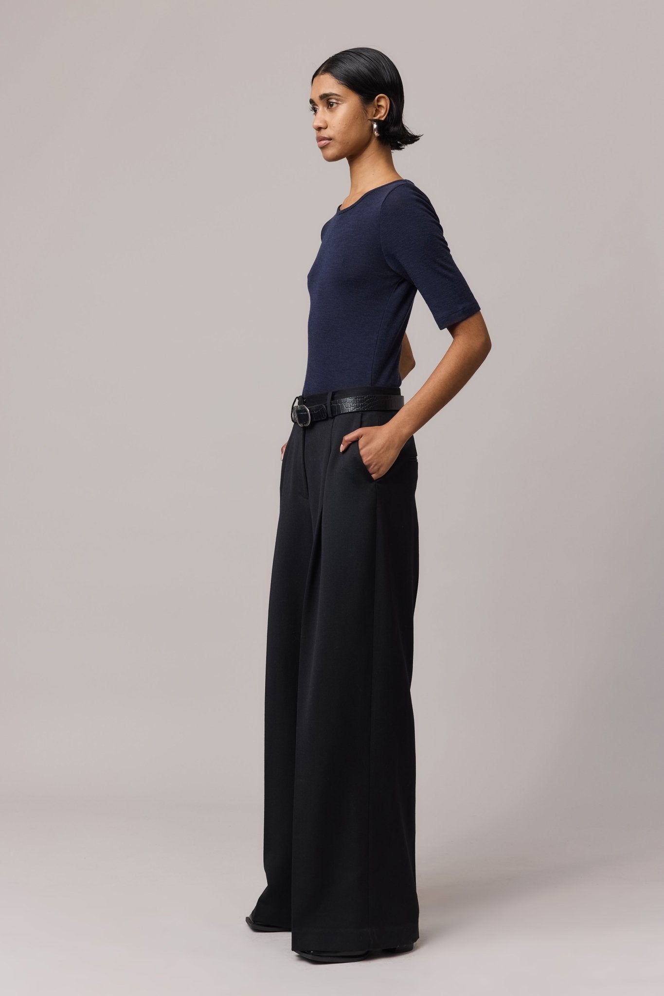 Side view of a woman wearing an indigo Merino Wool Crew Neck Tee with elbow sleeves and black linen pants.