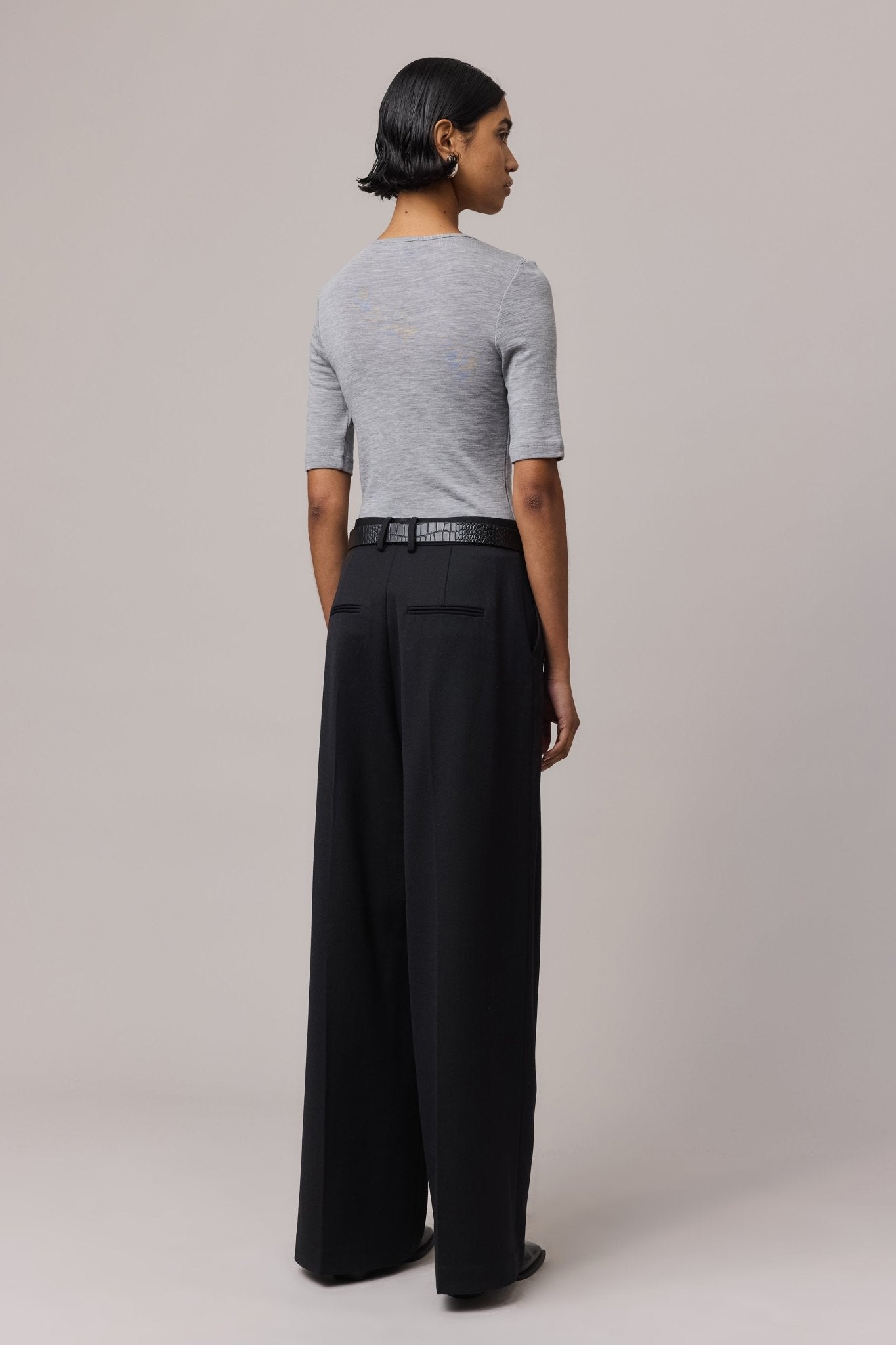 View from behind of a woman wearing a grey Merino Wool Crew Neck Tee with elbow sleeves and long black pants.