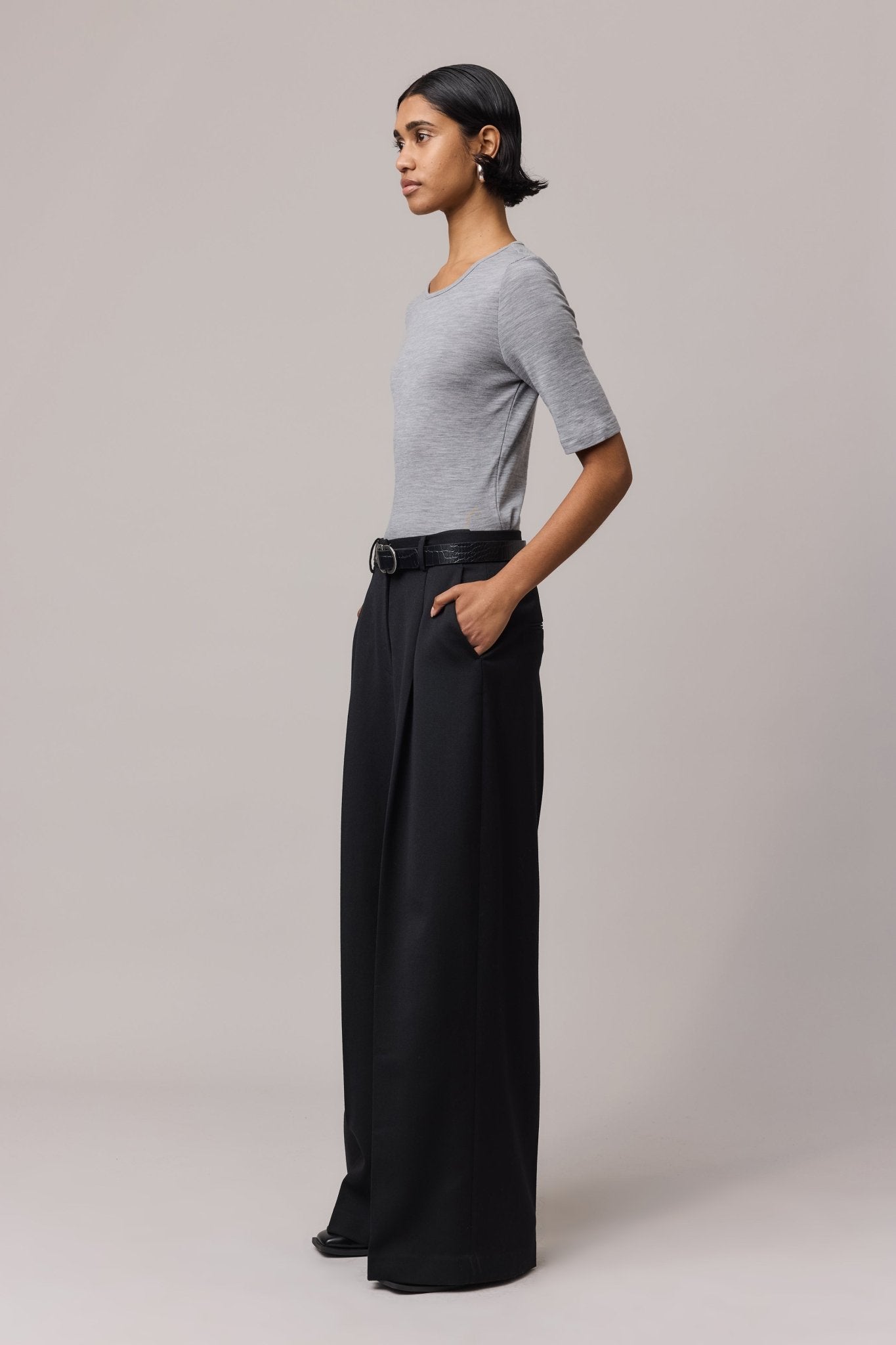 Side view of a woman wearing a grey Merino Wool Crew Neck Tee with elbow sleeves and long black pants.