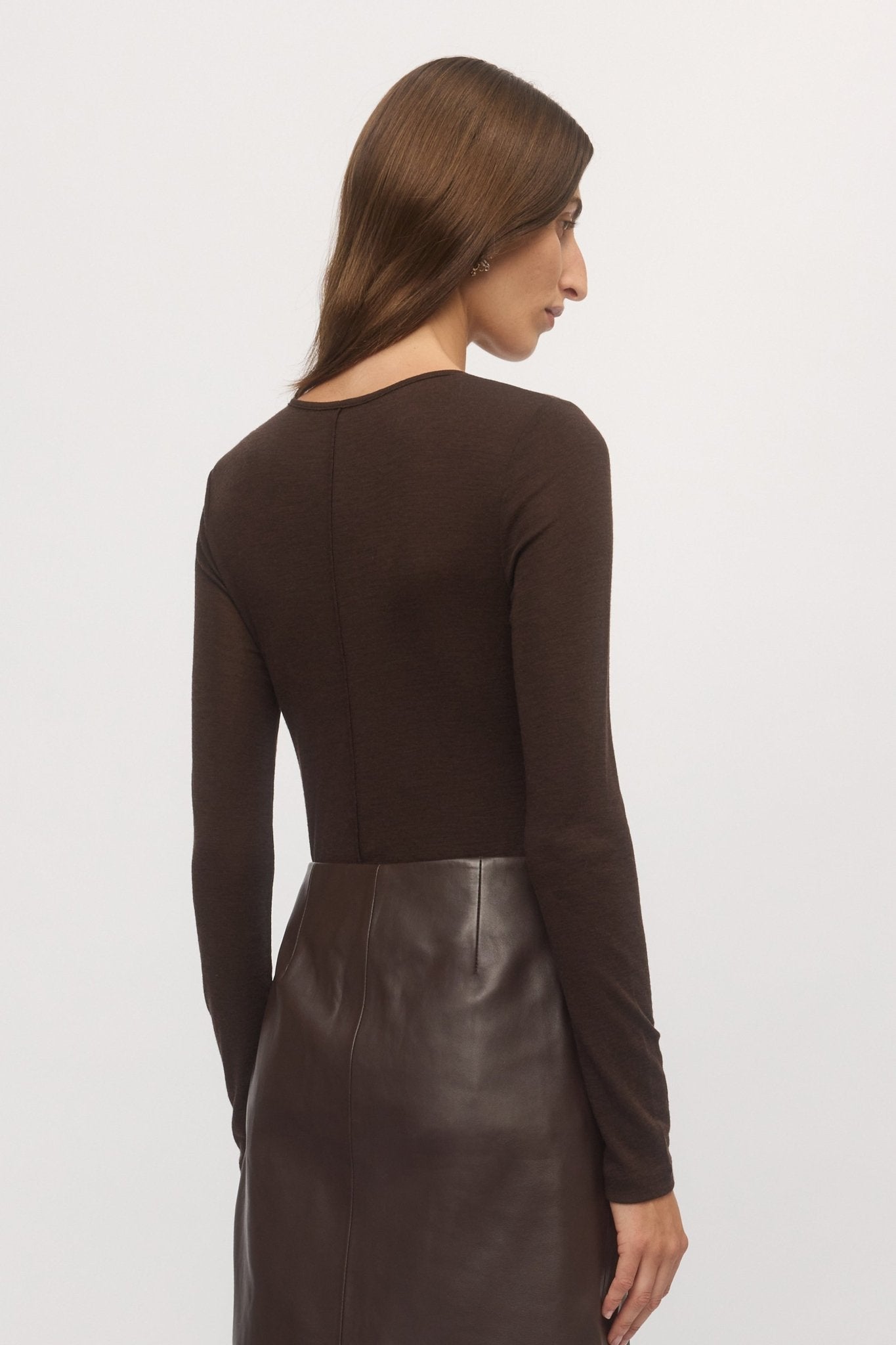 Close-up back view of woman wearing Merino V sweater in mahogany wool with brown leather mini skirt – Skin and Threads