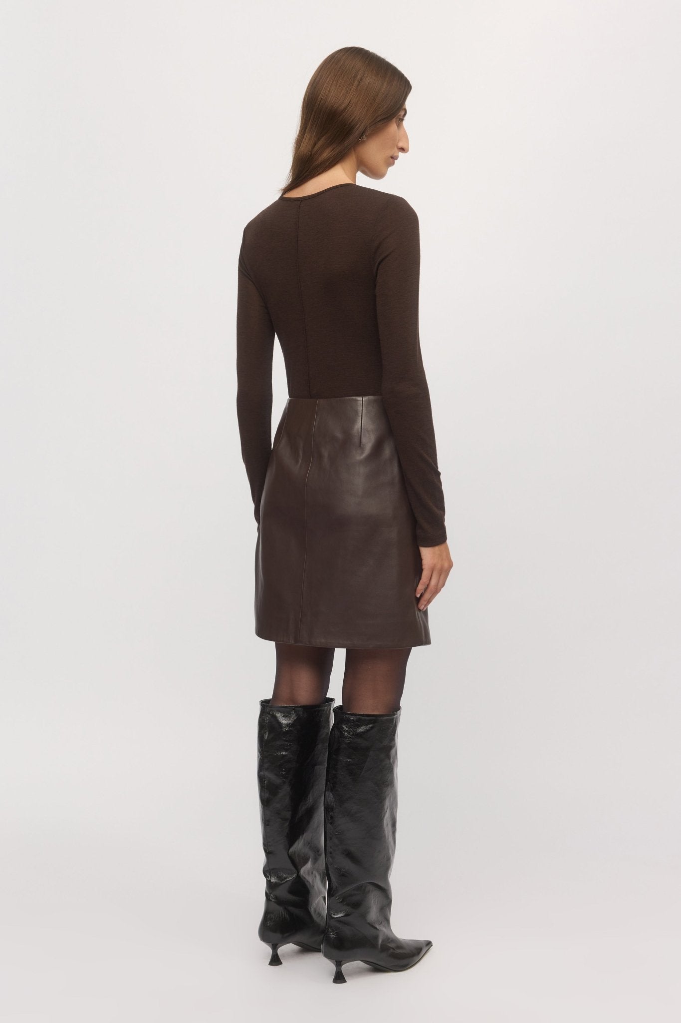 Back view of woman wearing Merino V mahogany sweater and leather skirt – Skin and Threads