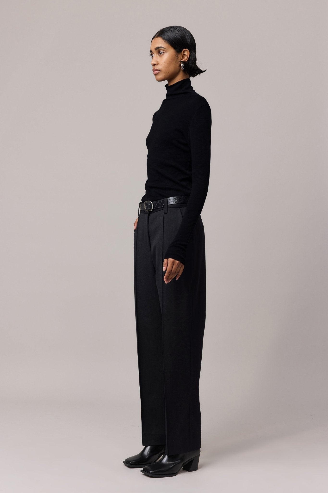 Side profile of a woman in a black Merino Wool Slim Fit Skivvy and black pants, highlighting the skivvy's slim, flattering cut and comfortable stretch.