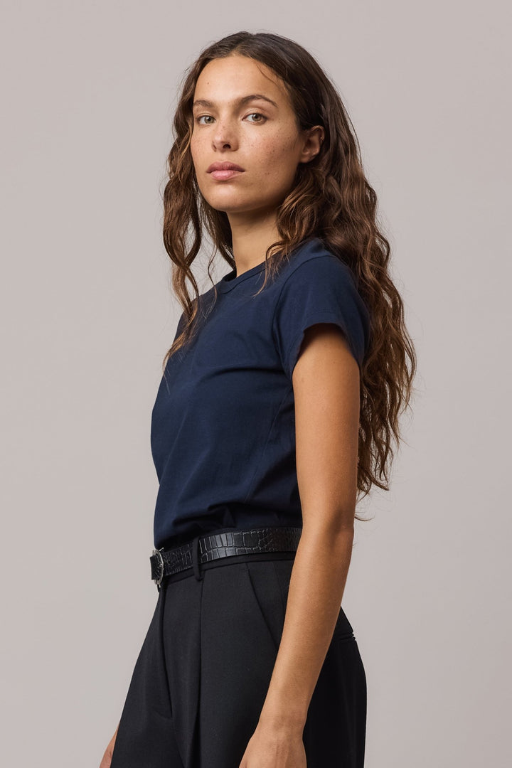 A woman wearing a indigo blue organic cotton girlfriend tee with a classic crew neck, paired with black high-waisted trousers.