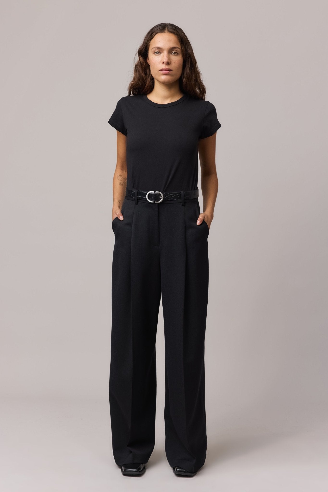 A woman wearing a classic black organic cotton tee with a crew neck and relaxed fit, paired with black wide-leg trousers.