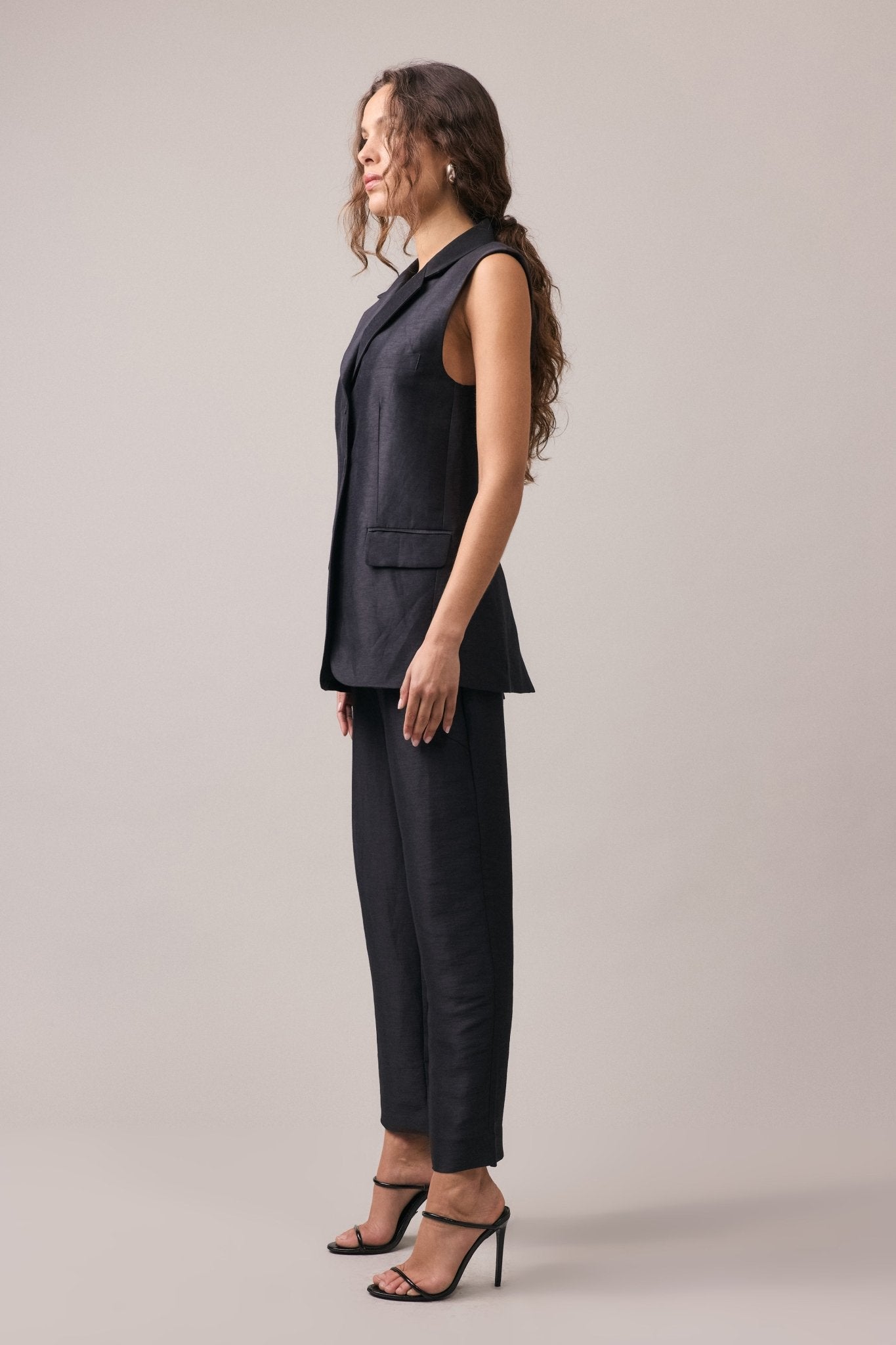 Woman wearing the Remi Silk Linen Pant with the matching longline vest, seen from the side, showcasing the slimline leg profile and relaxed fit.