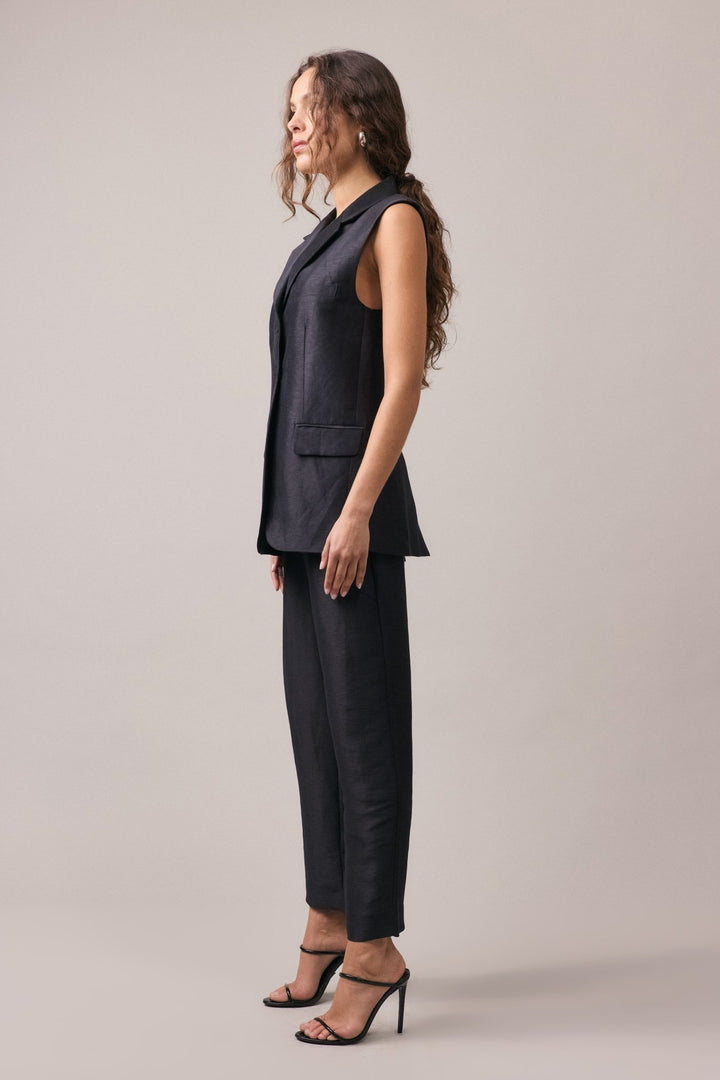 Woman seen from the side wearing the Remi Silk Linen Vest, showcasing the front pocket detail and the vestโs longline profile.