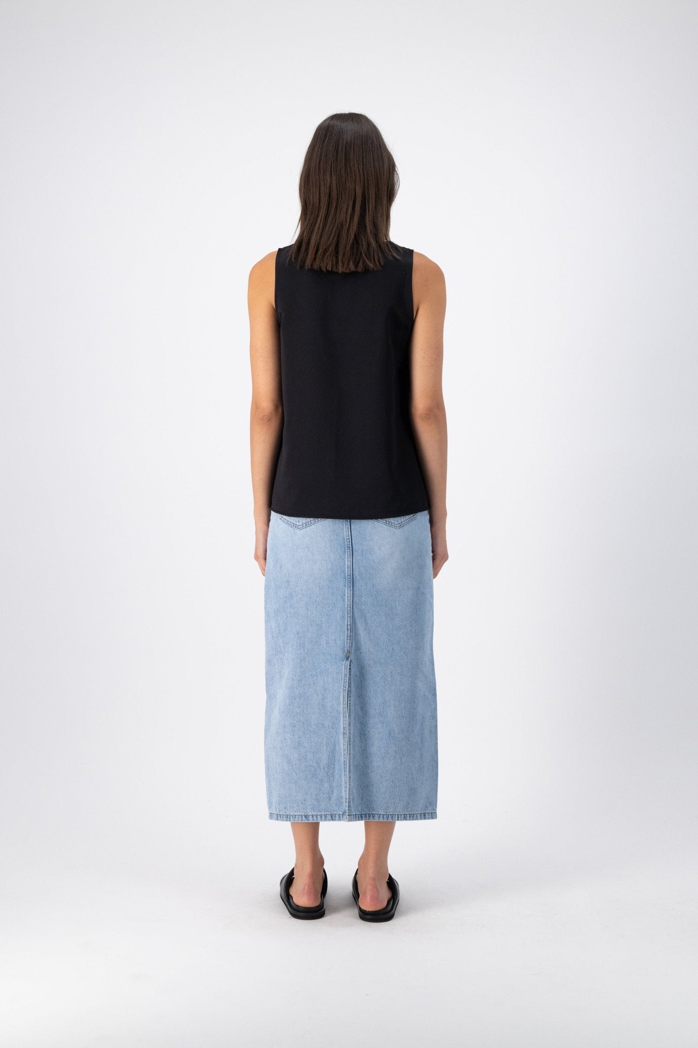 Back view of a woman wearing a black wool-silk tank top, highlighting the wide straps and relaxed fit, paired with a denim skirt.
