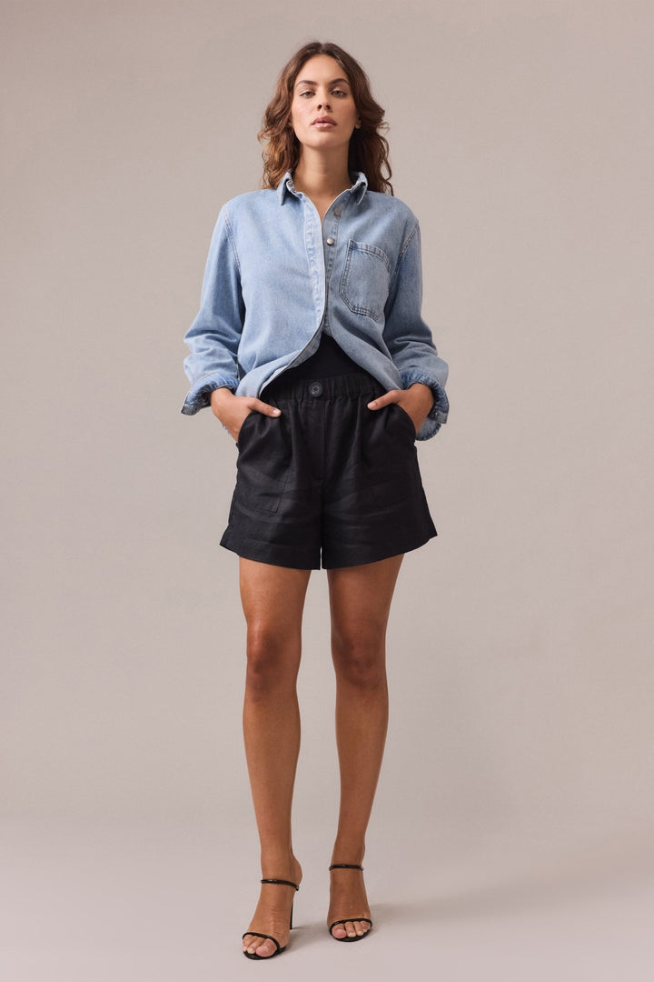 A woman is wearing black Soma linen shorts paired with a denim shirt.