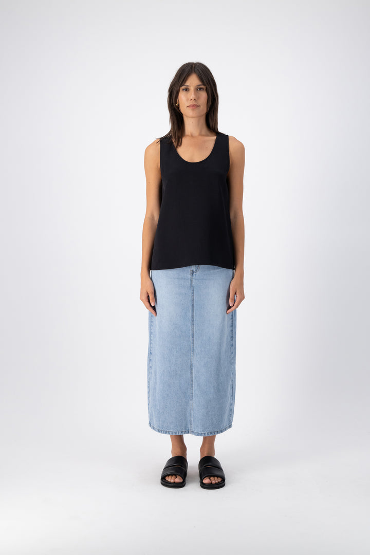 A woman styled in a black wool-silk tank top and a long denim skirt, showcasing a versatile and elegant casual outfit.