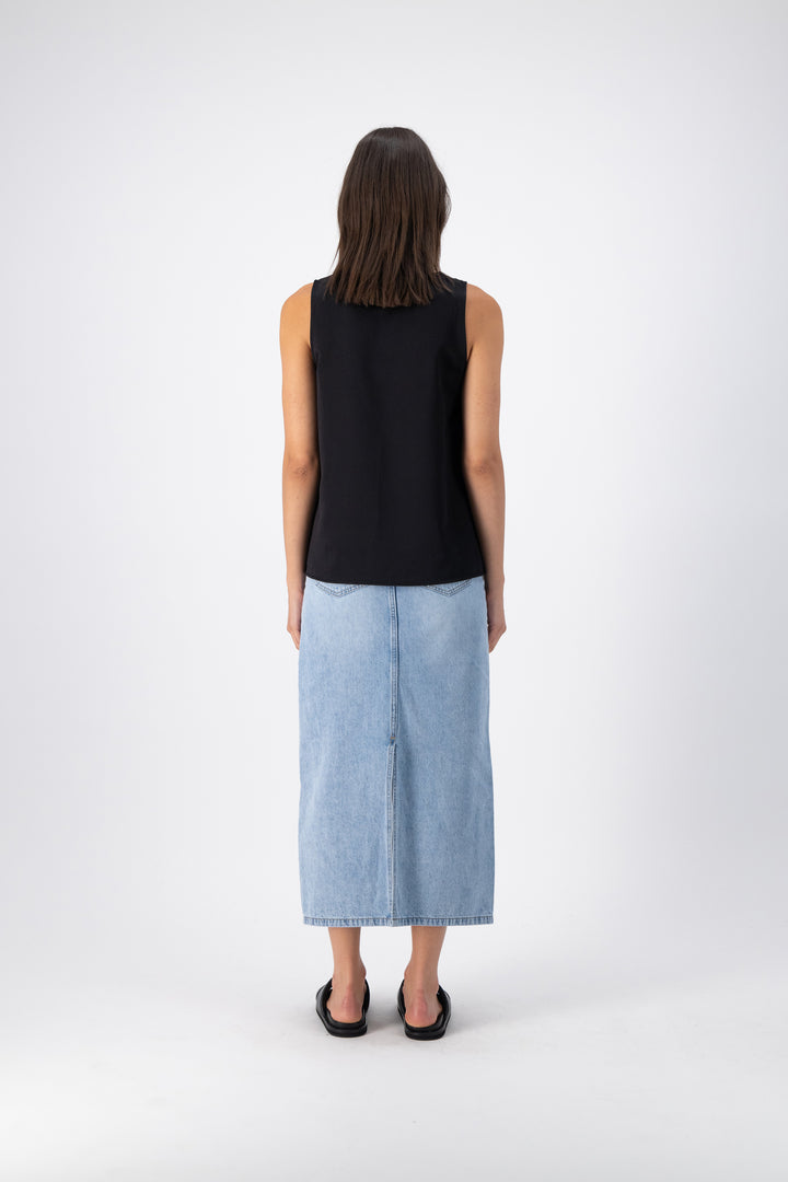 Back view of a woman wearing a black wool-silk tank top, highlighting the wide straps and relaxed fit, paired with a denim skirt.