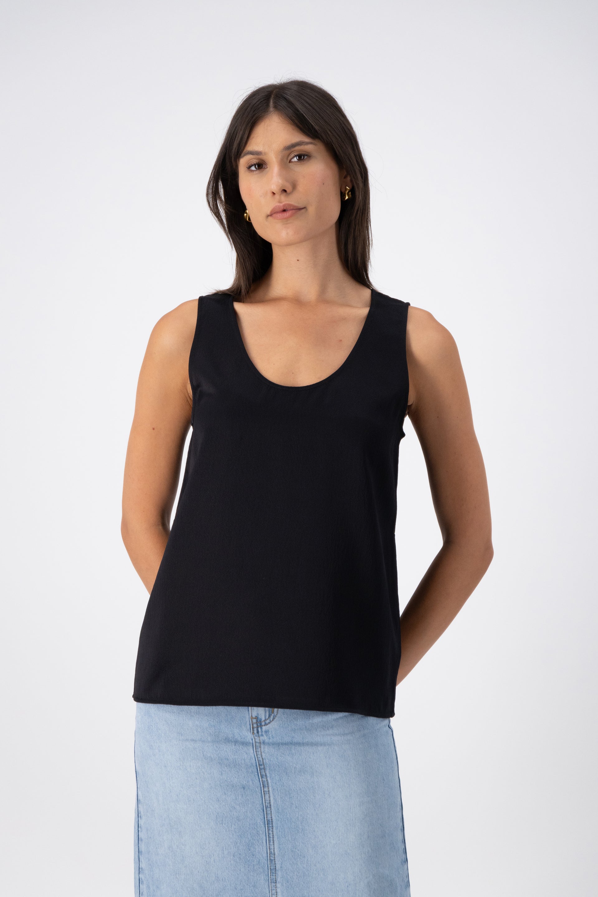 A woman wearing a black wool-silk tank top with a relaxed fit, U/V-shaped neckline, and wide straps, paired with a denim skirt.