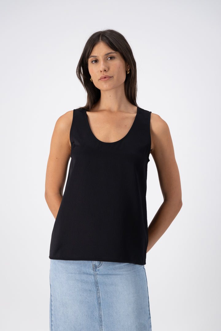 A woman wearing a black wool-silk tank top with a relaxed fit, U/V-shaped neckline, and wide straps, paired with a denim skirt.
