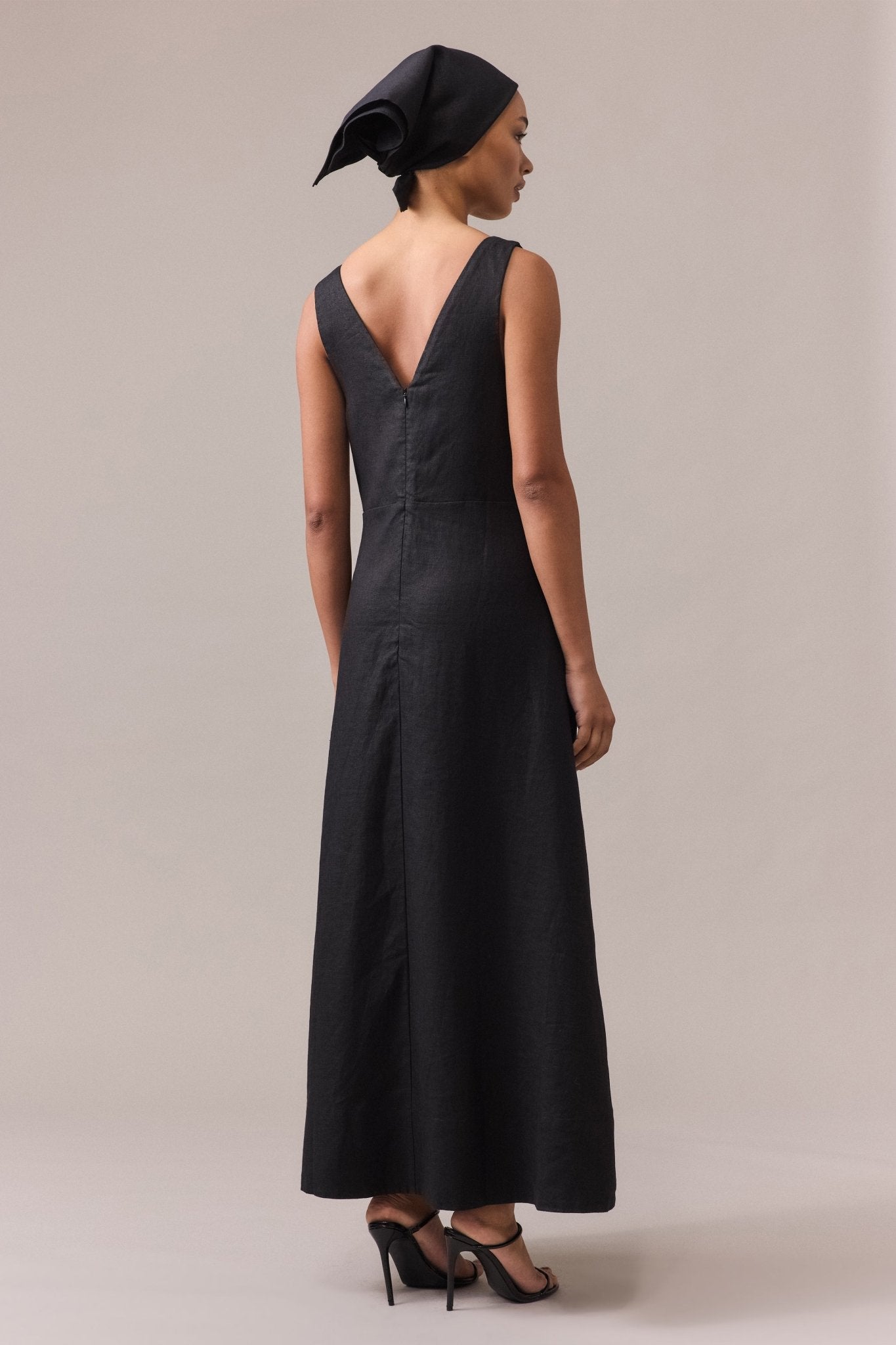 A woman seen from the back, wearing the black Alessandra Linen Maxi Dress paired with black sandals.