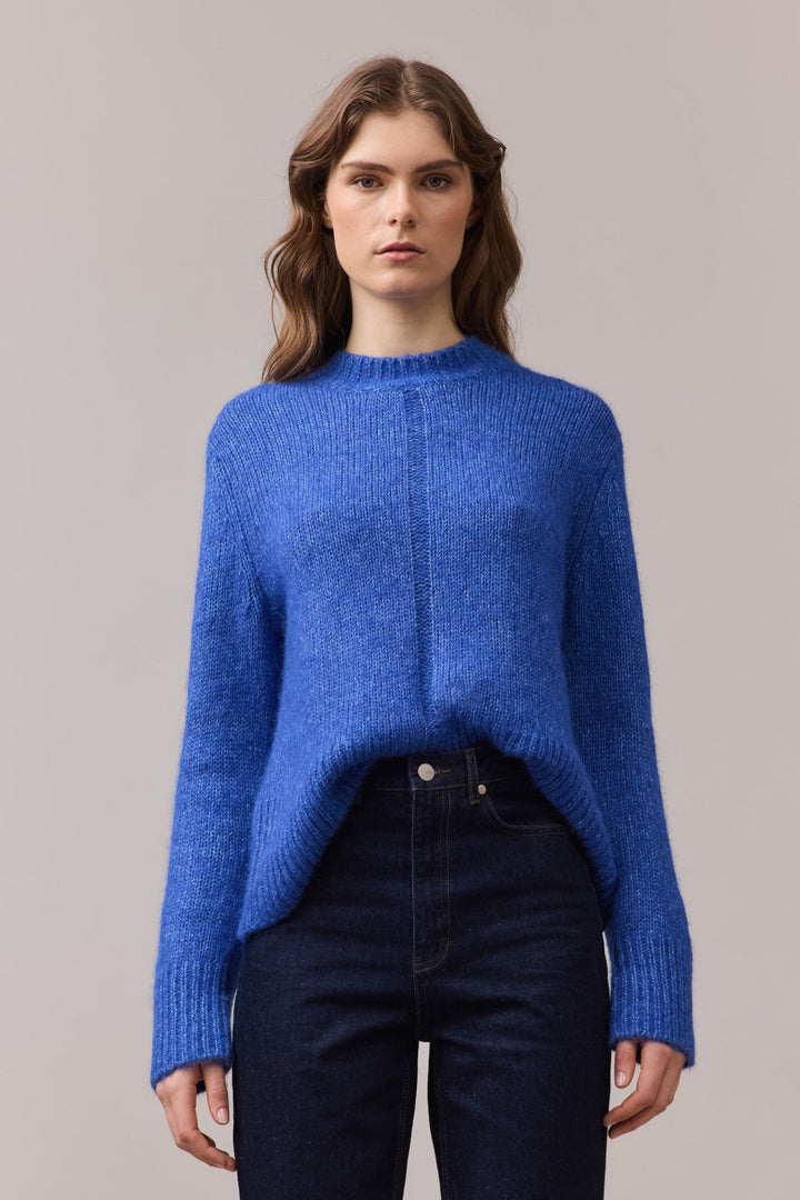 Woman wearing the Alfie Alpaca Cotton Knit in cobalt blue, styled with a front tuck into high-rise jeans, highlighting the ribbed hem and soft drape.