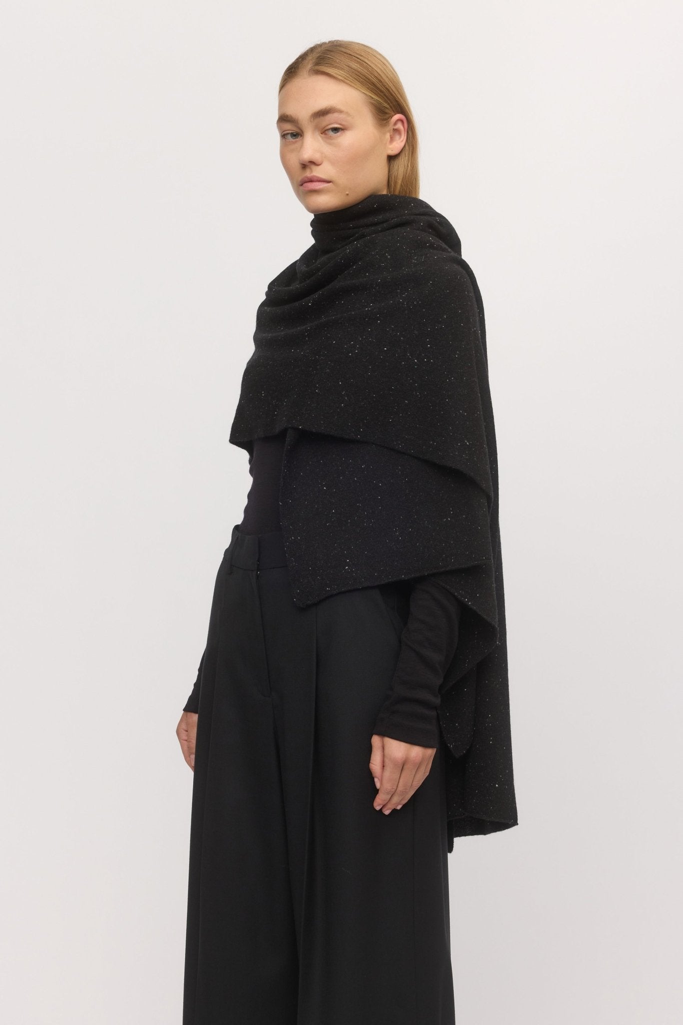 Woman in side profile wearing the Anywhere Wrap in Stargaze – dark wool-cashmere wrap layered over a black outfit, from Skin and Threads.