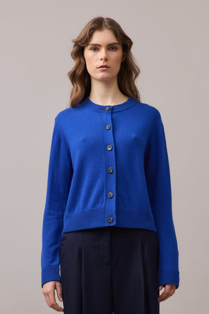 Front view of a woman in a 100% cashmere cardigan in cobalt blue, styled with long sleeves and feature buttons for a clean, timeless look.