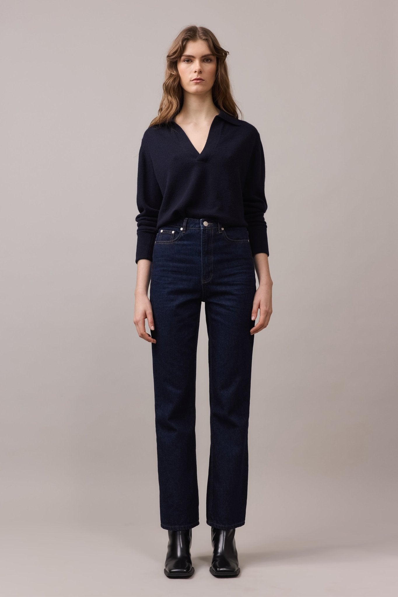 Woman wearing the Cashmere Polo Knit in 100% cashmere, paired with dark blue high-waist jeans. The relaxed fit polo features a V-neck with collar and long sleeves, showcasing its everyday luxury design.