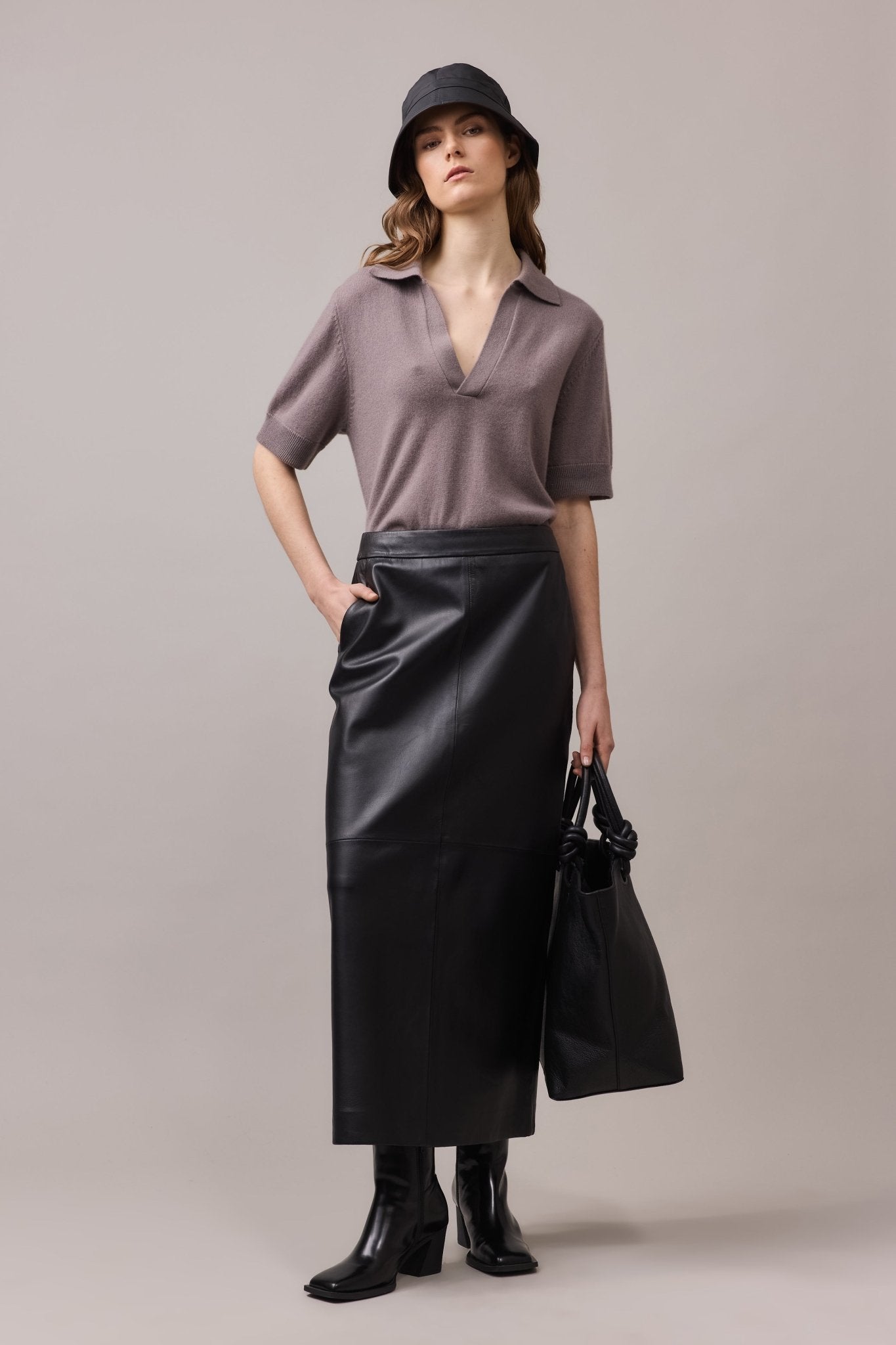 Front view of the woman wearing the relaxed-fit, Cashmere Polo Tee paired with a maxi leather skirt, one hand in her pocket, and accessorized with a black hat for a chic and timeless look.