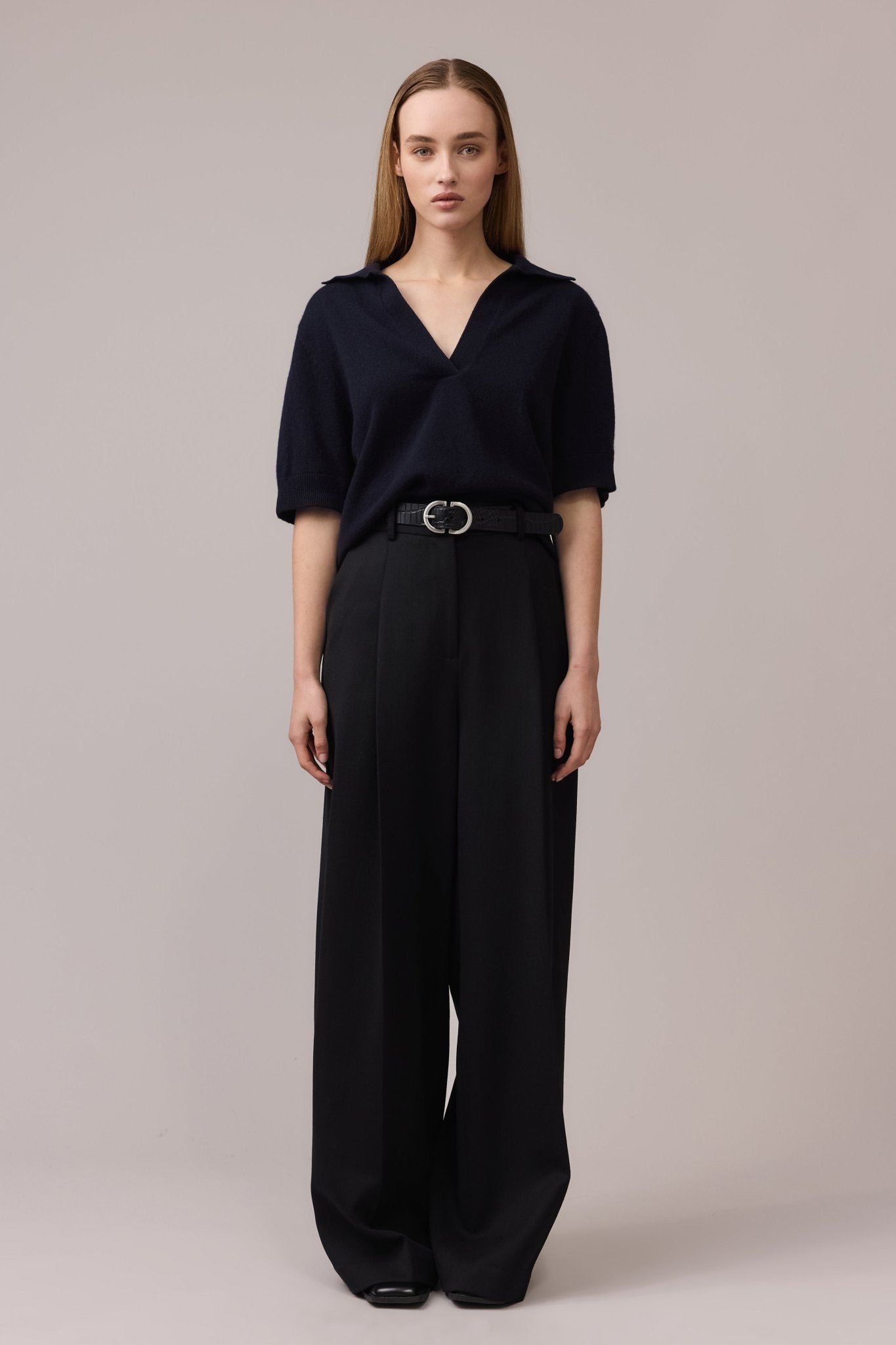 Woman wearing the navy Cashmere Polo Tee tucked into black linen wide-leg pants, with a belt visible. The V-neck collar and relaxed fit of the tee complement the casual yet refined look.