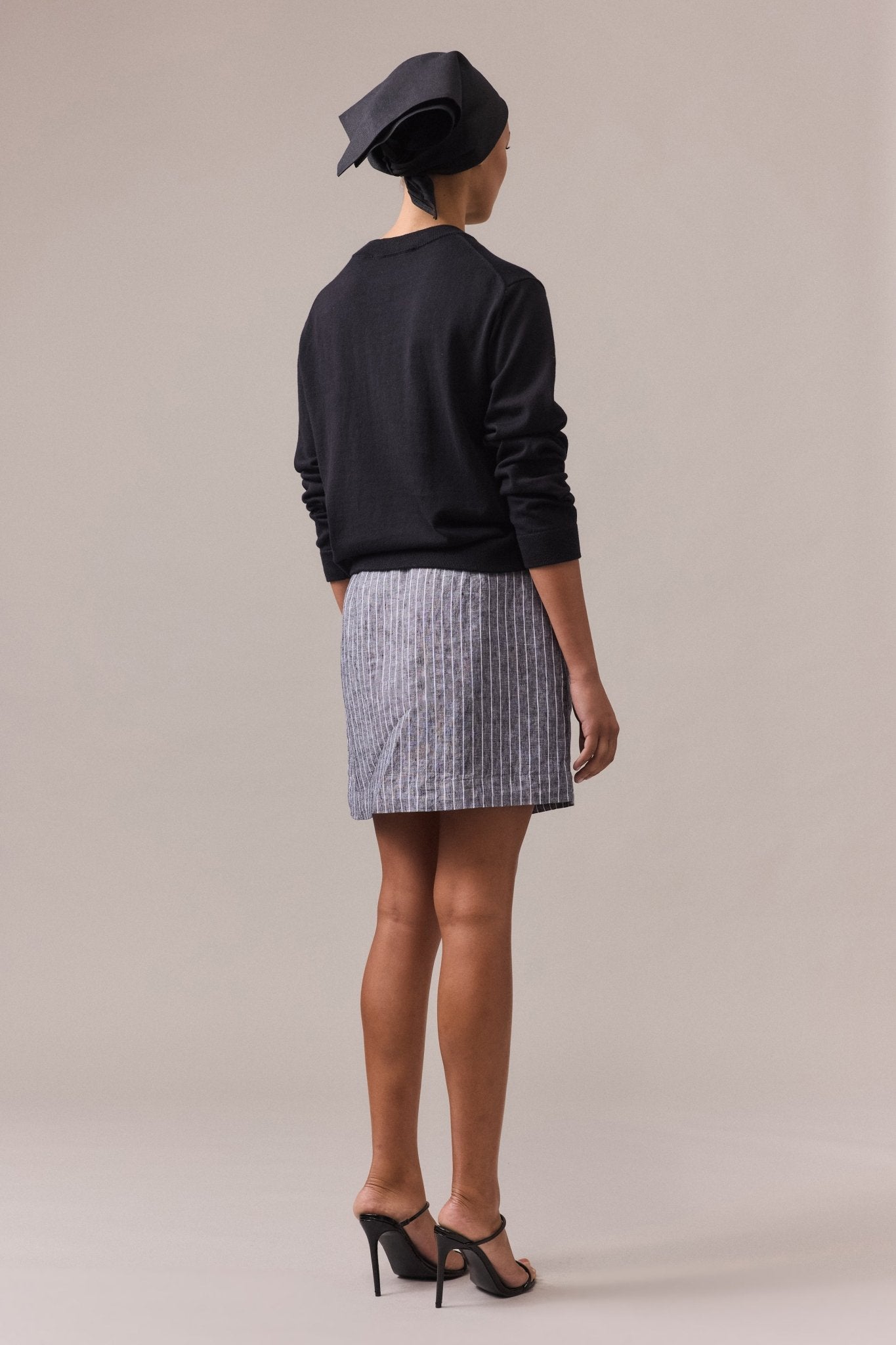 A woman seen from the back, wearing a black cotton-cashmere crew neck knit paired with a grey skirt.