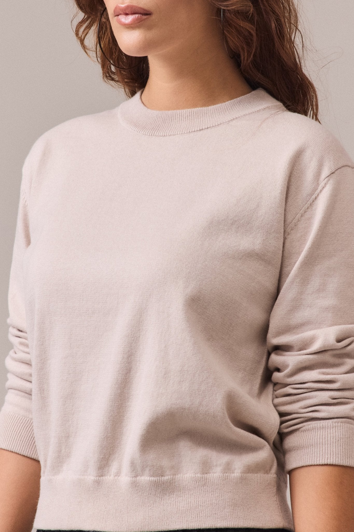 A woman in a sand cotton-cashmere crew neck knit with long sleeves.