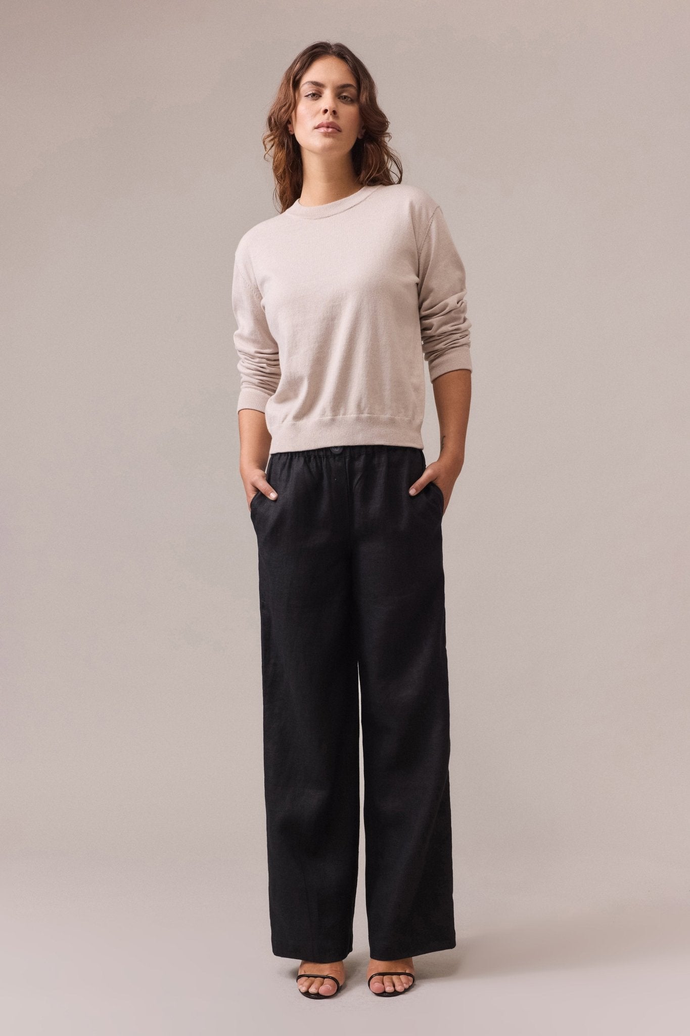 A woman wearing a sand cotton-cashmere crew neck knit with long sleeves, paired with long wide-leg black pants.