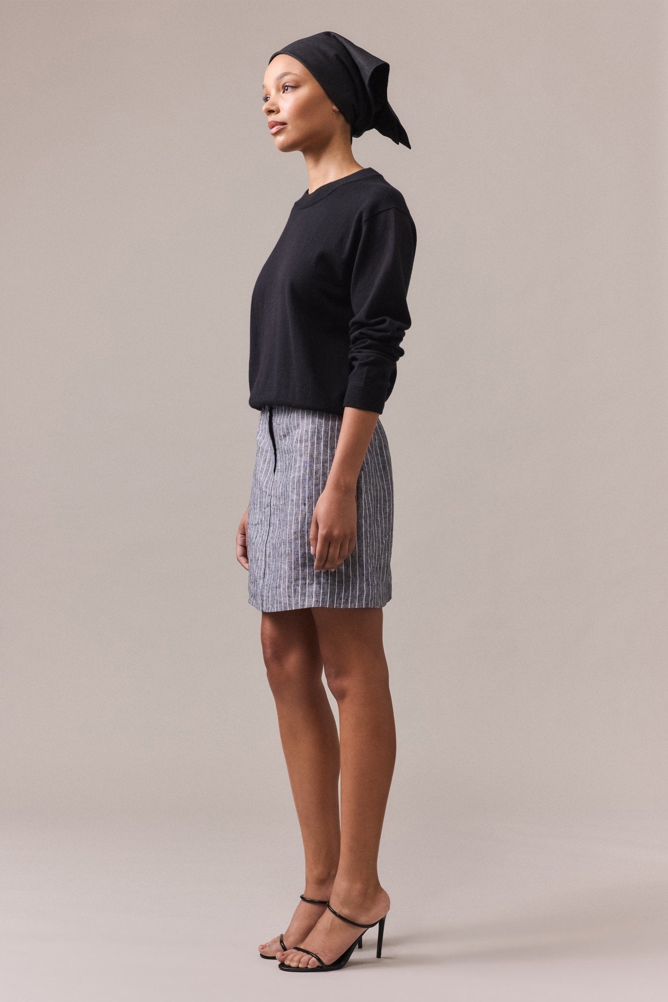 A woman in a black cotton-cashmere crew neck knit, paired with a grey skirt.