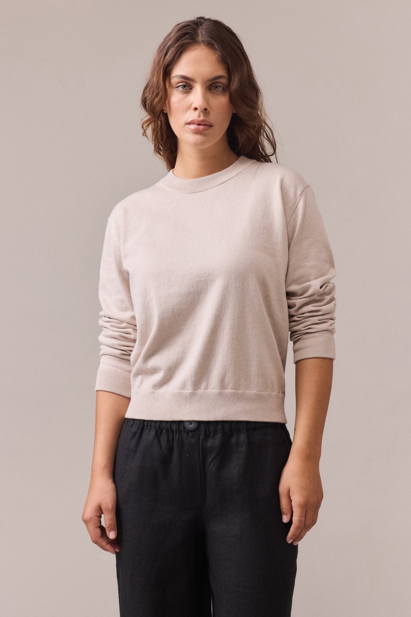 A woman wearing a sand cotton-cashmere crew neck knit with long sleeves.